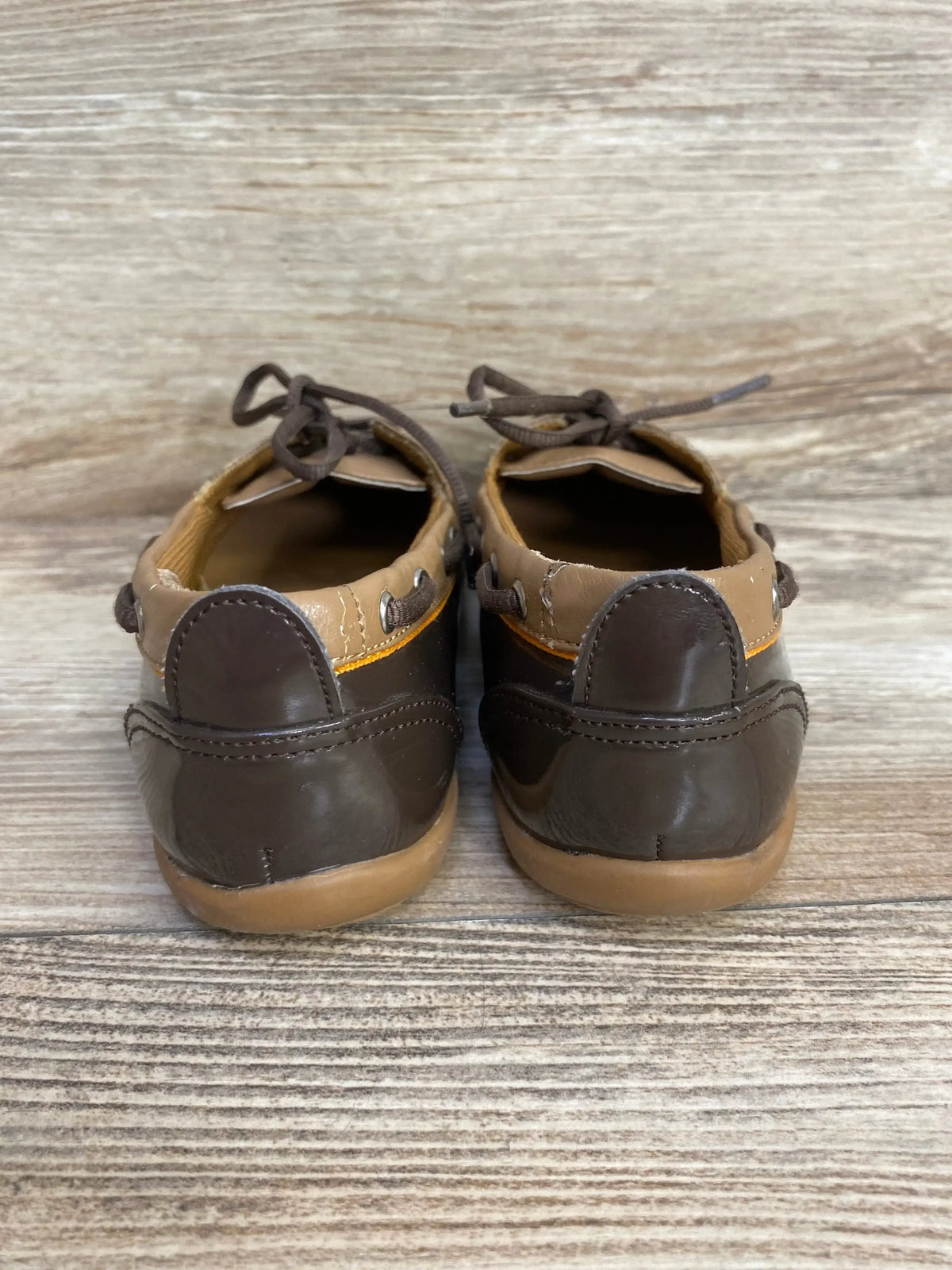 Rear view of toddler Balleto brown boat shoes showcasing stitched heel detail and lace ties on wood background