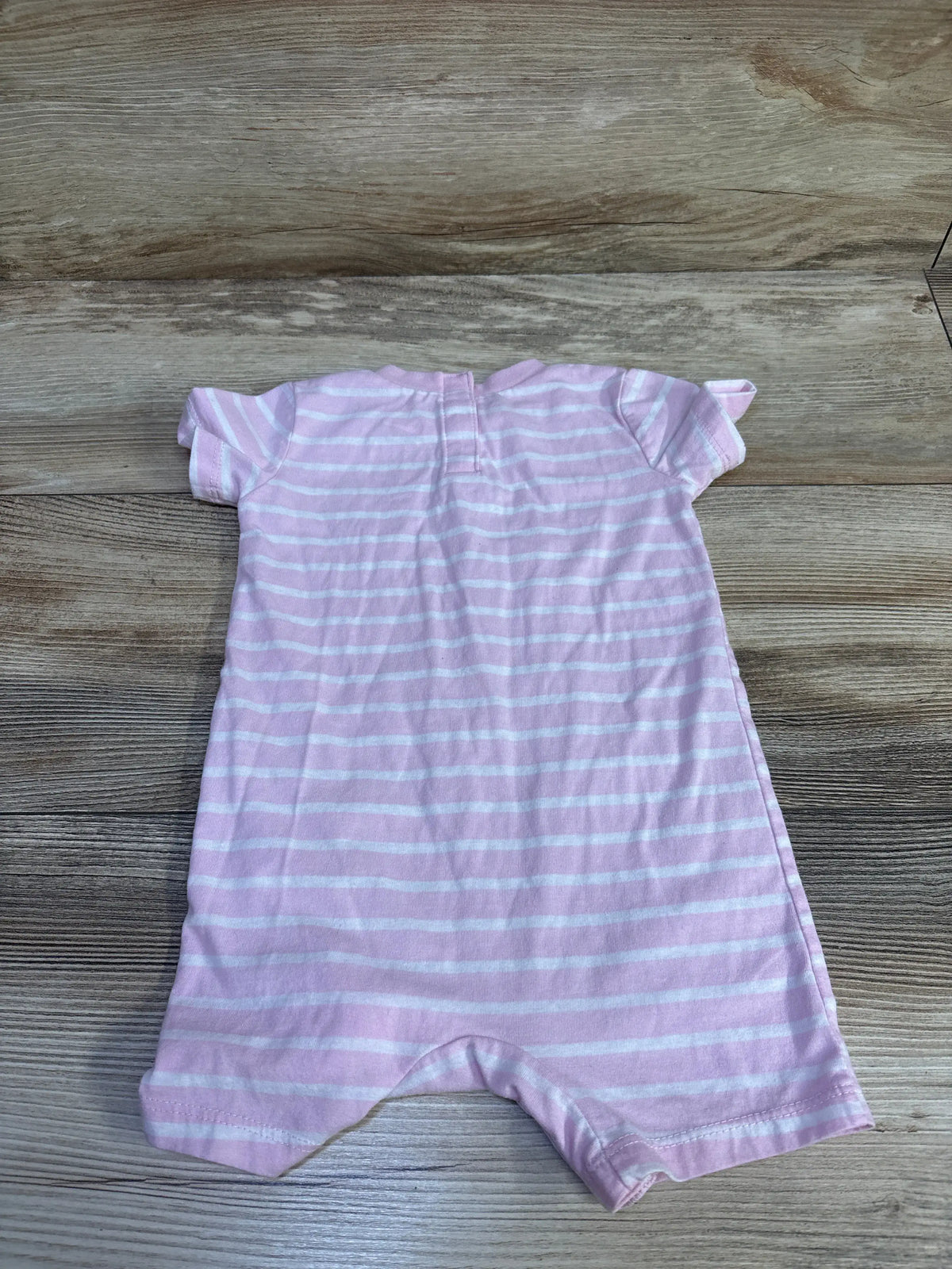 Flat lay of Nike pink striped shortie romper showcasing short sleeves and enclosed legs with a wood-grain background