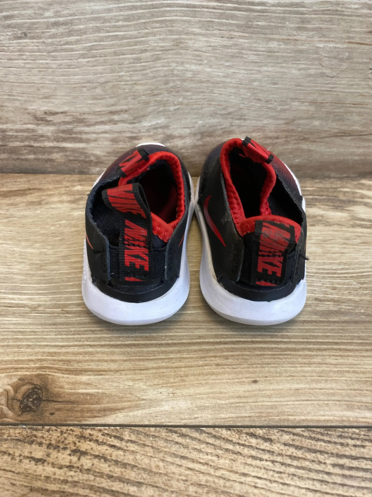 Rear view of Flex Runner TD sneakers showcasing black and red slip on uppers with white foam soles on a wood surface