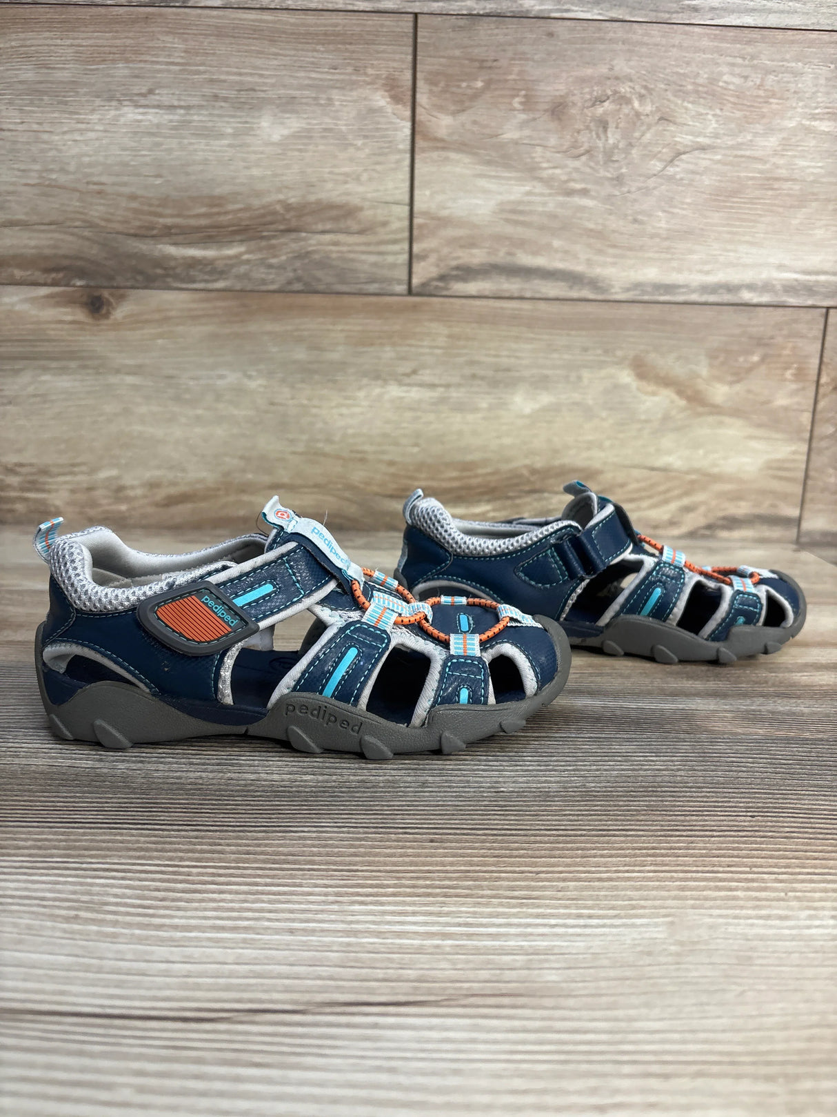 Navy blue boys’ closed-toe sandals with orange and teal accents on wood background