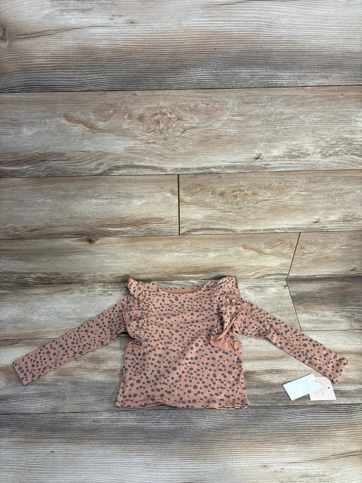 Top view of brown Grayson Mini ruffled polka dot top, size 4T, with shoulder ruffles on a wood floor