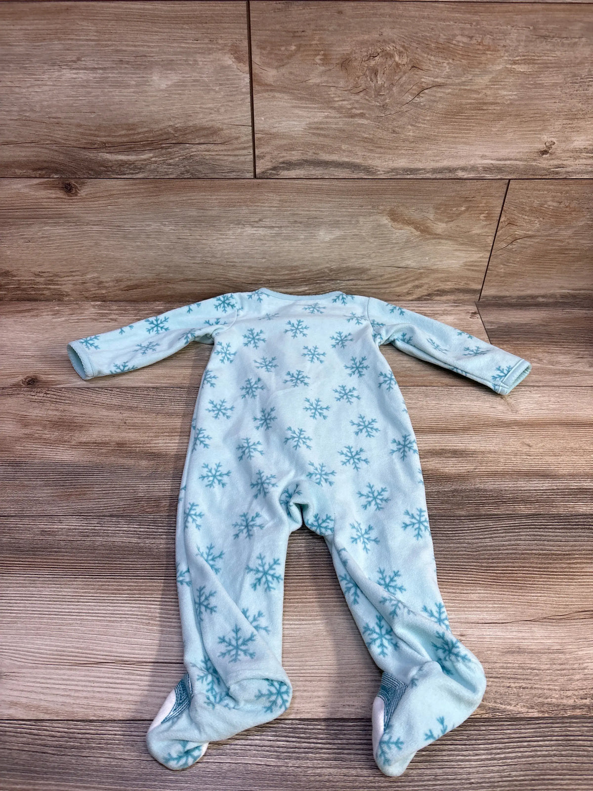 Front view of Just One You blanket sleeper showcasing blue snowflake pattern and covered feet with a wood backdrop