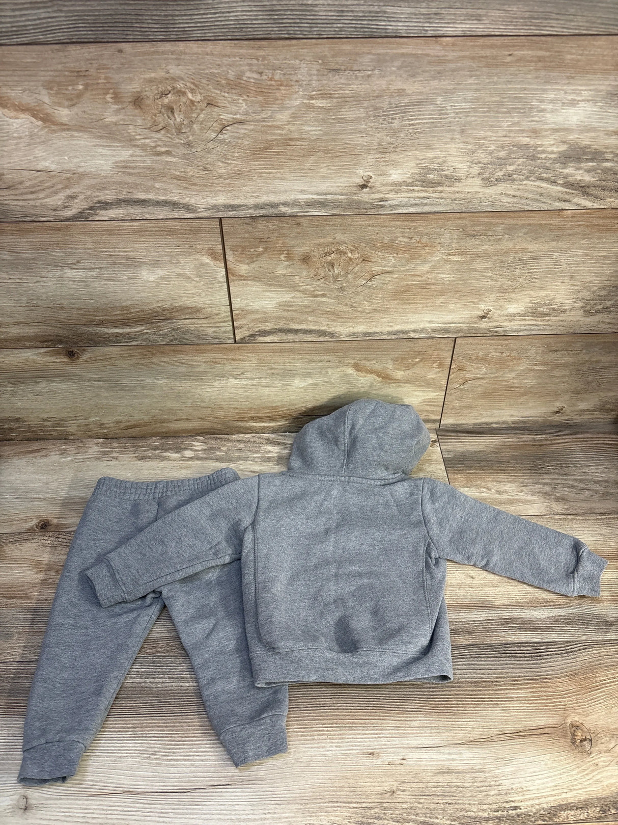 Top-down view of grey Champion 2-piece toddler hoodie and joggers, back of hooded pullover showing small dark stain, on wood floor, size 18 months