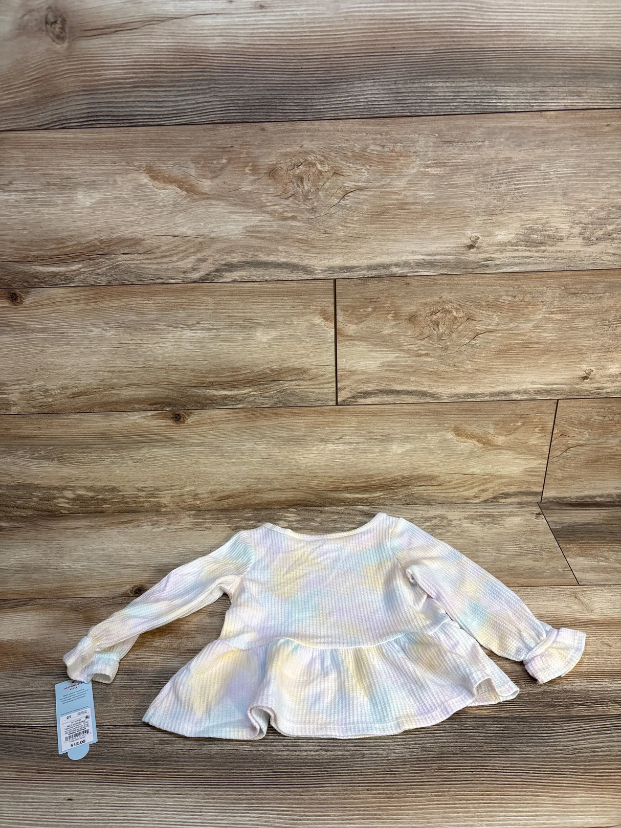 Long sleeve pastel tie-dye baby shirt with ruffle hem displayed on wood background
