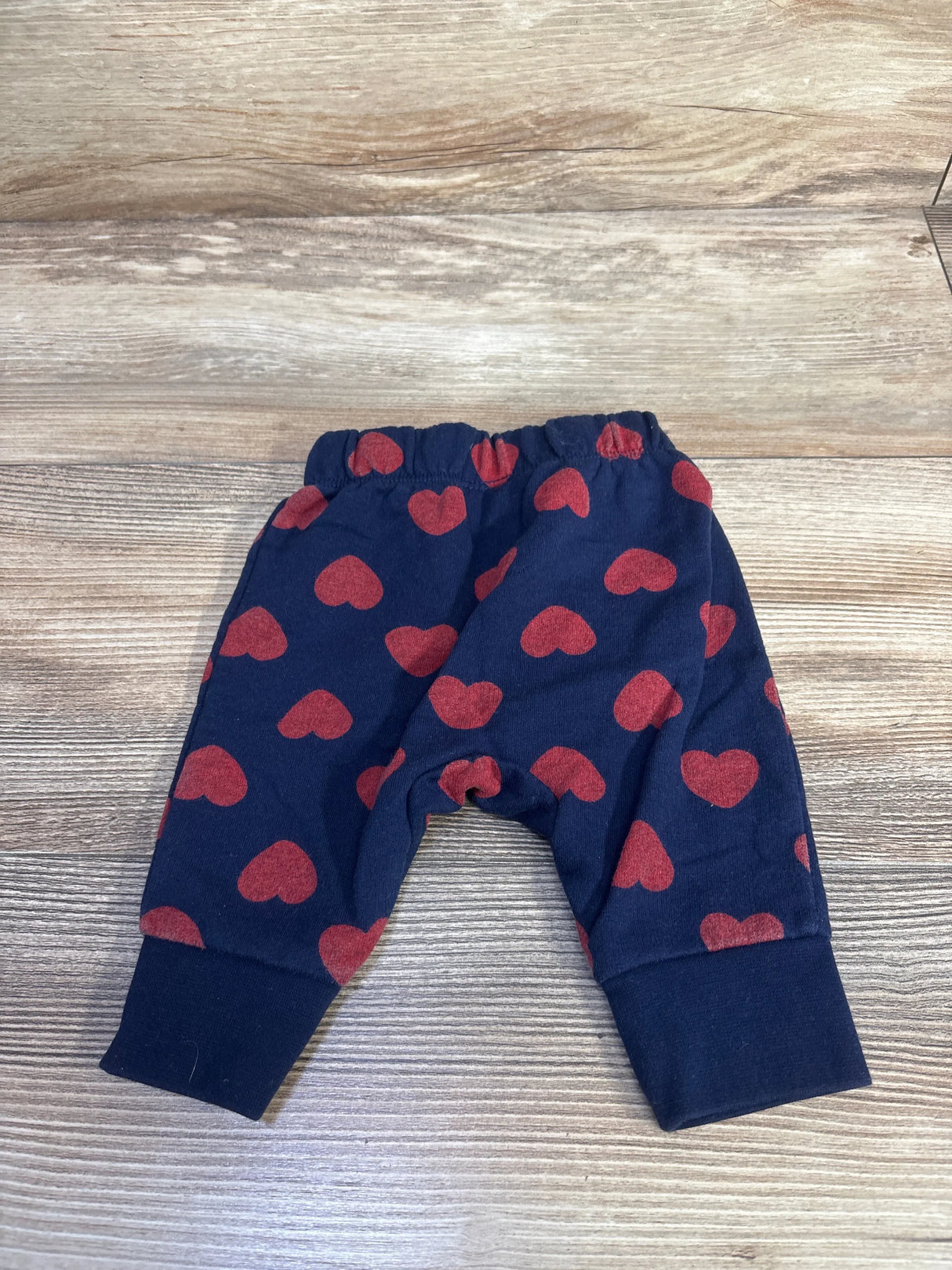 Front flat-lay of Cat & Jack navy newborn joggers showcasing red heart print and elastic waistband on light wood background
