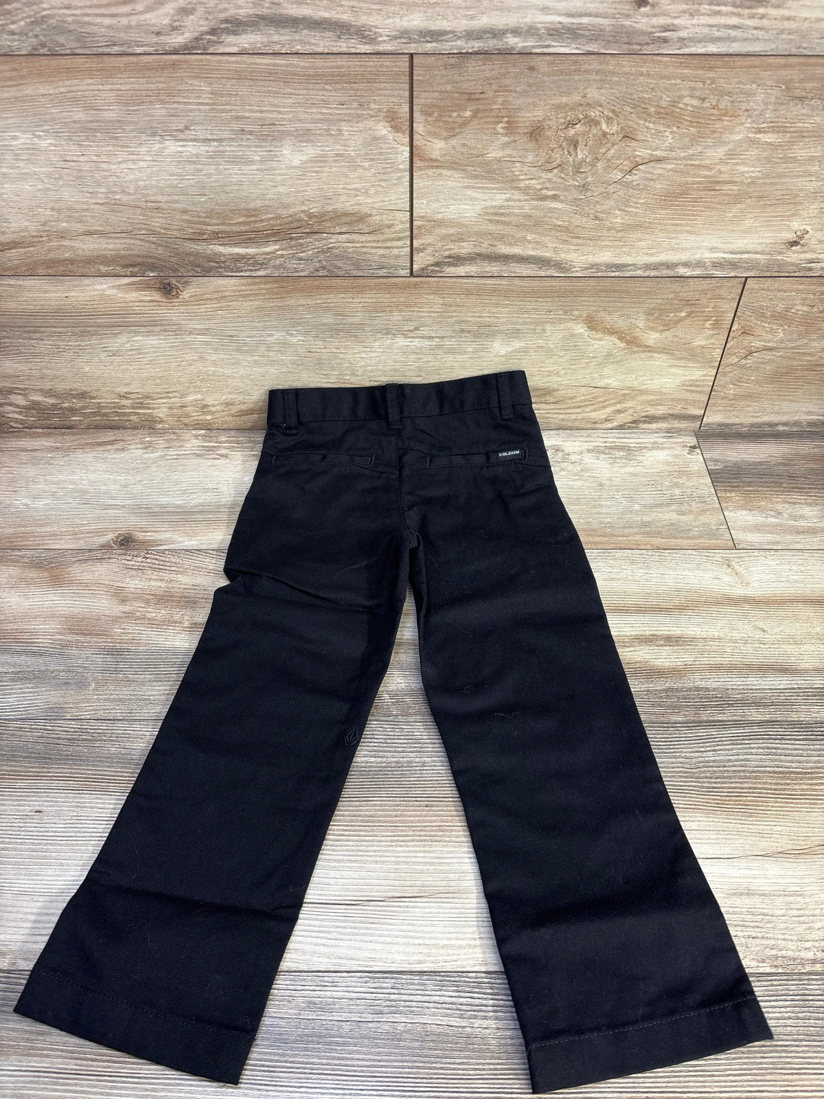 Front view of black Volcom VMonty pants showcasing belt loops and front pockets on a wood plank background
