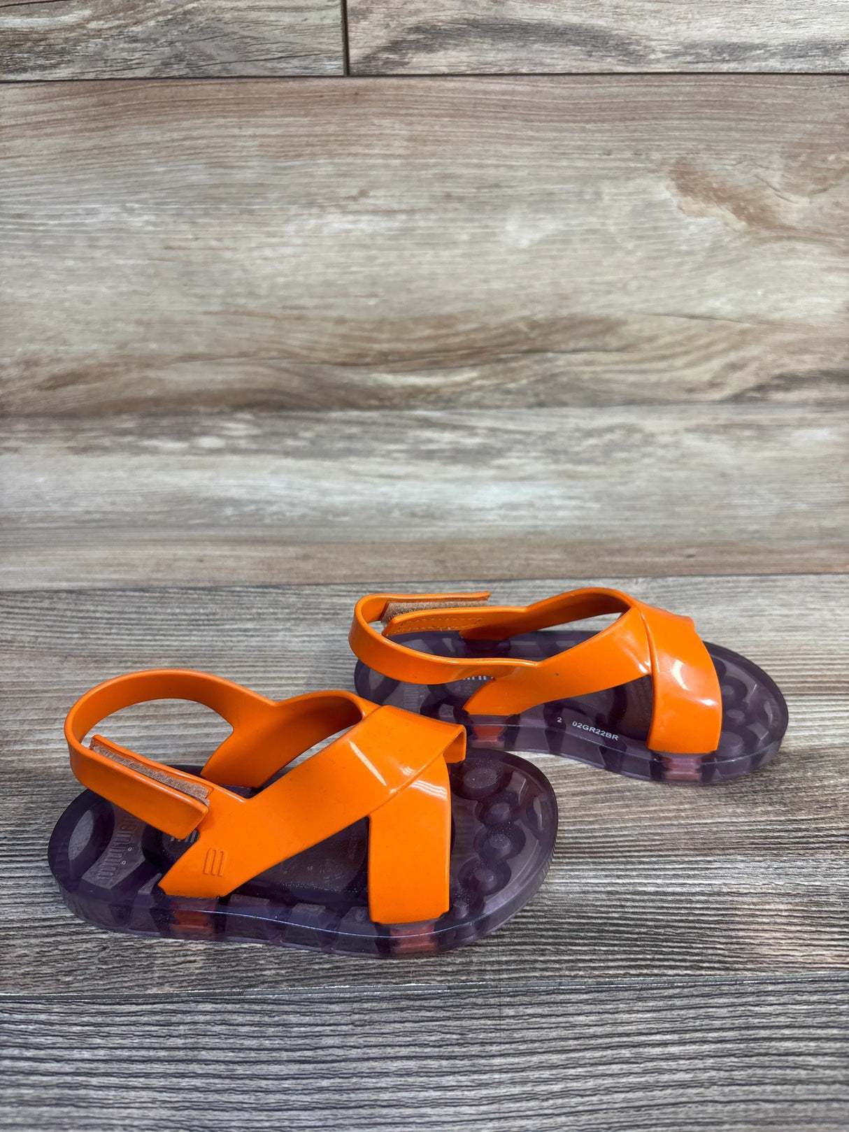 Orange toddler sandals with crisscross straps and clear soles on wood background