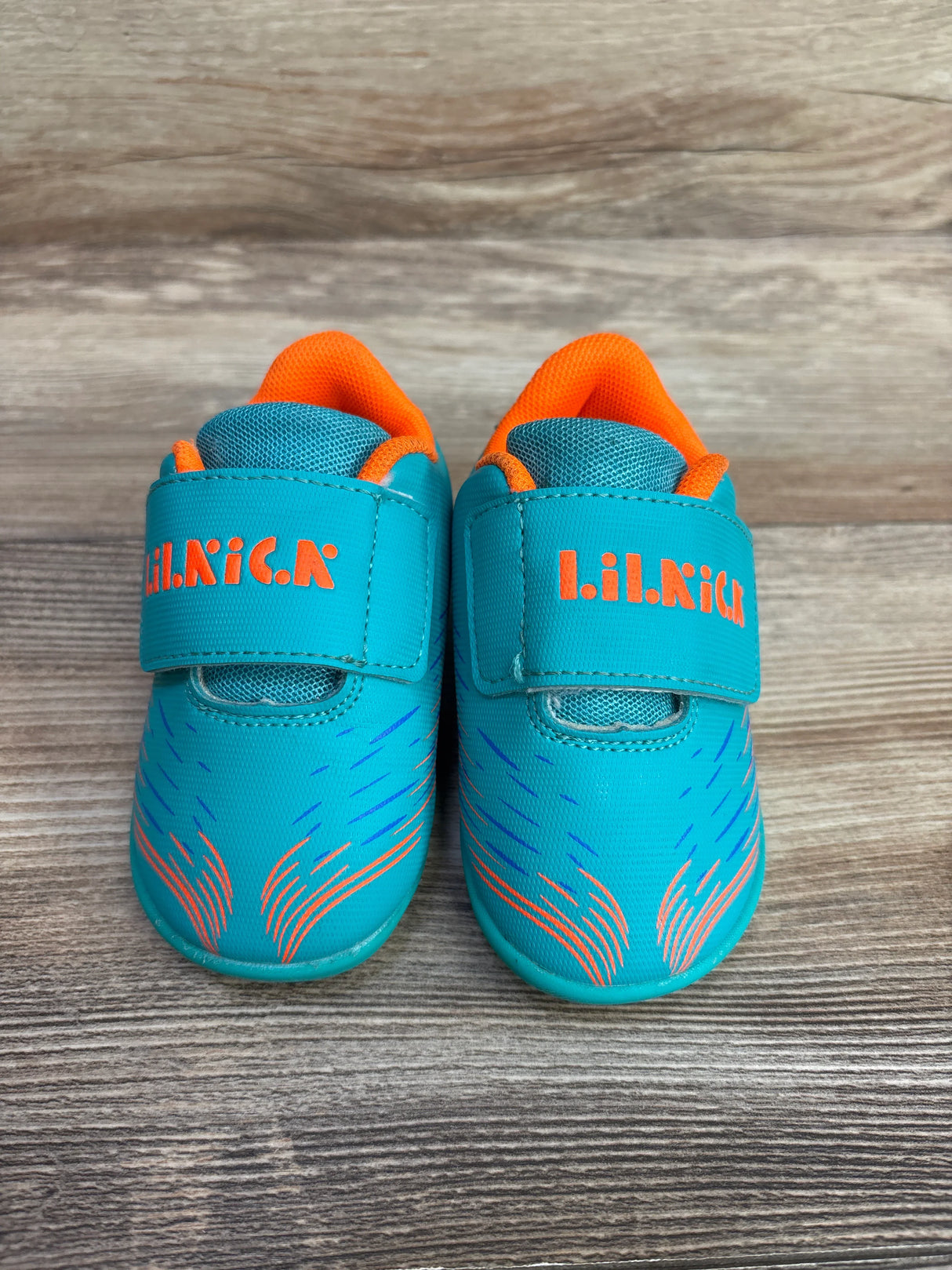 Pair of turquoise and orange Lil Nick toddler shoes with velcro straps on wooden floor