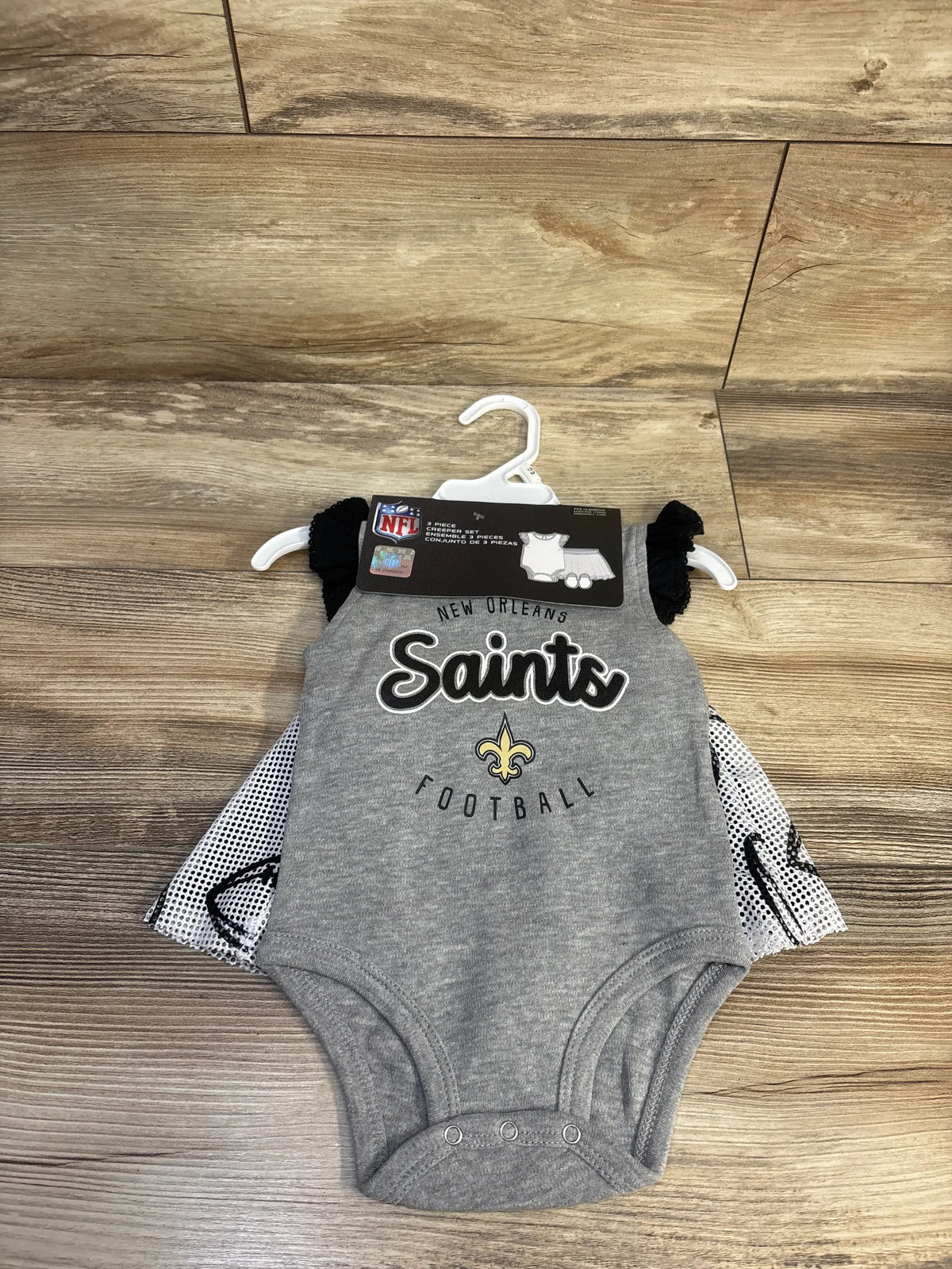 Front view of a gray New Orleans Saints three-piece creeper set showcasing Saints football graphics on a wood-look floor