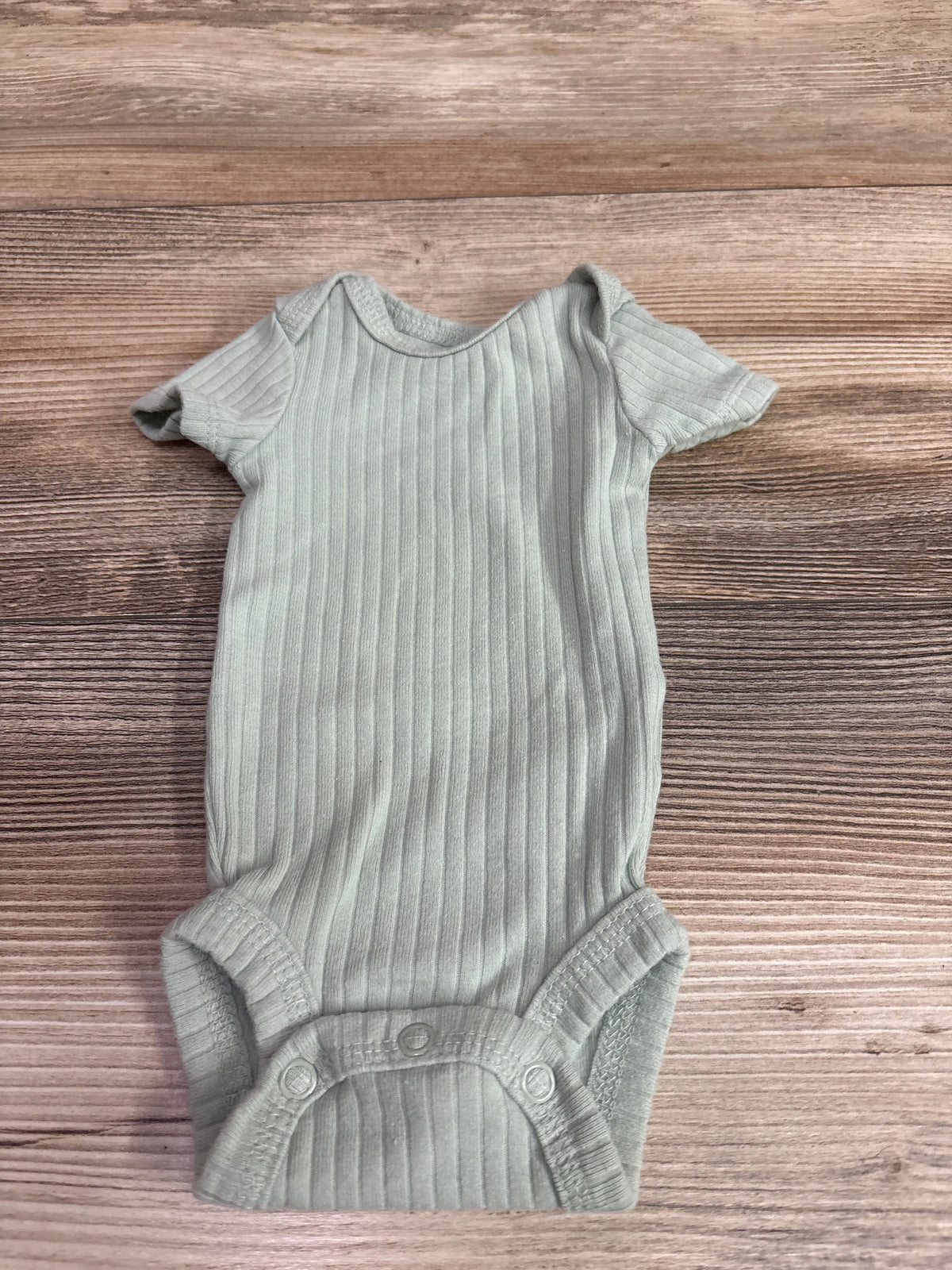 Top view of green Just One You ribbed bodysuit showcasing short sleeves and snap closure on a wood background