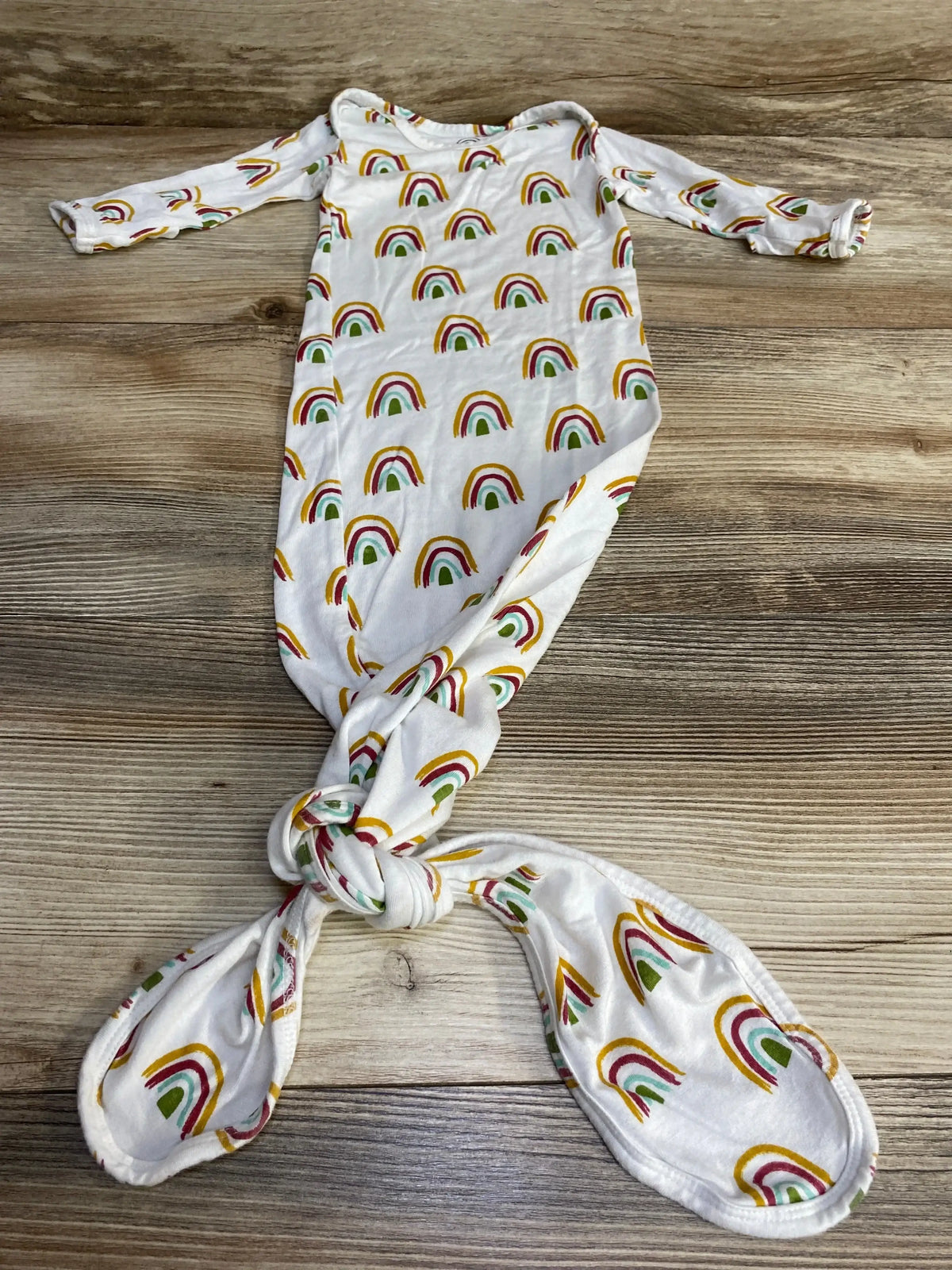 Top-down view of Emerson and Friends white newborn knot gown showing multicolored rainbow print, long sleeves, and tied knot bottom on wood background