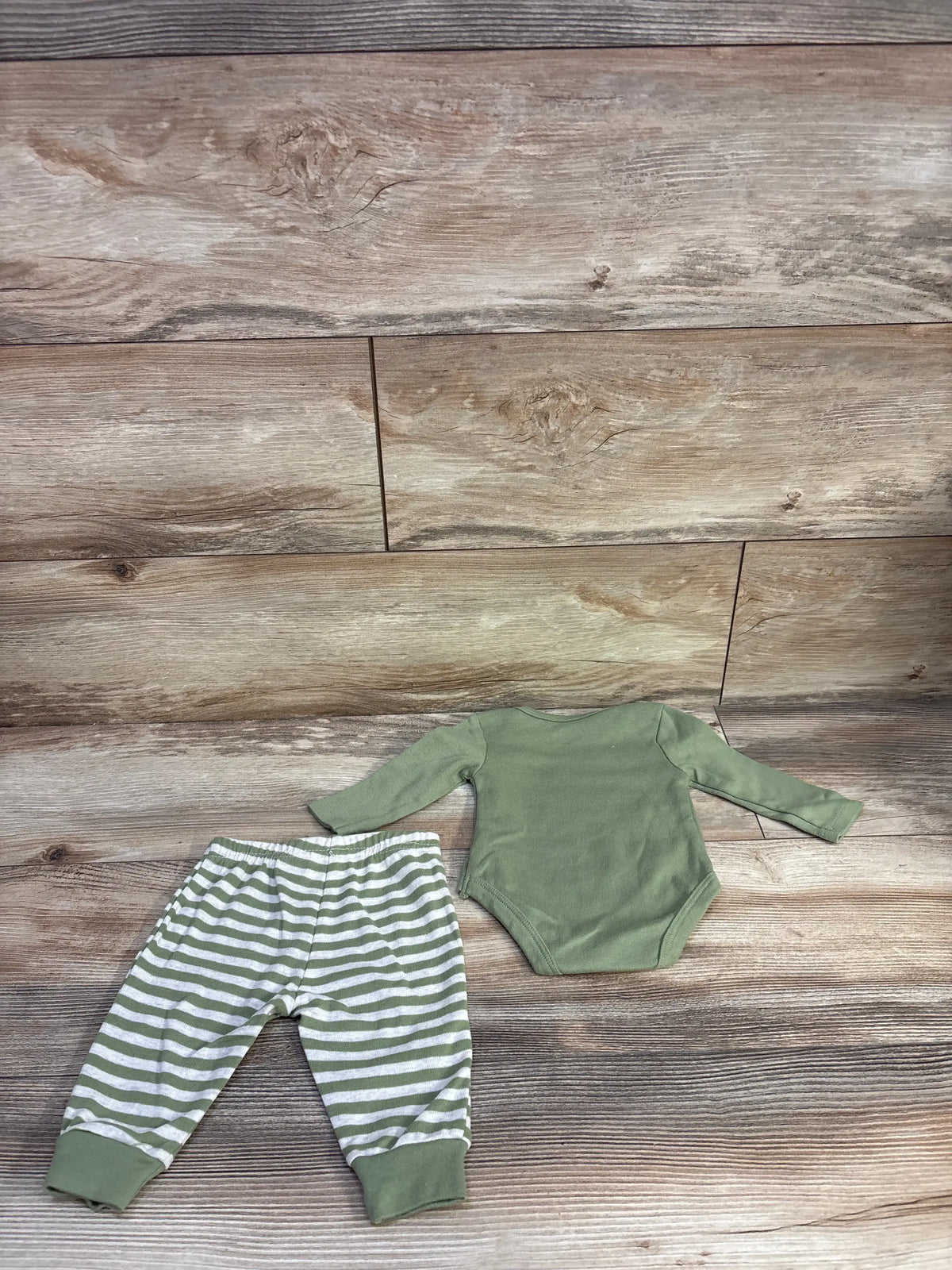 Flat lay of 2-piece baby set showcasing long-sleeve green bodysuit and green-and-white striped pants, size 3M on wood background