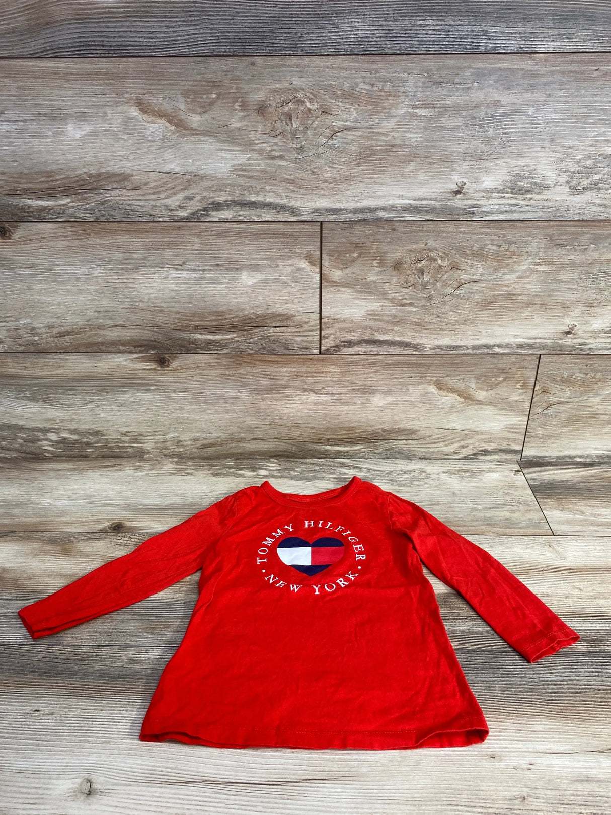 Red long sleeve toddler shirt with Tommy Hilfiger New York heart logo on wood background