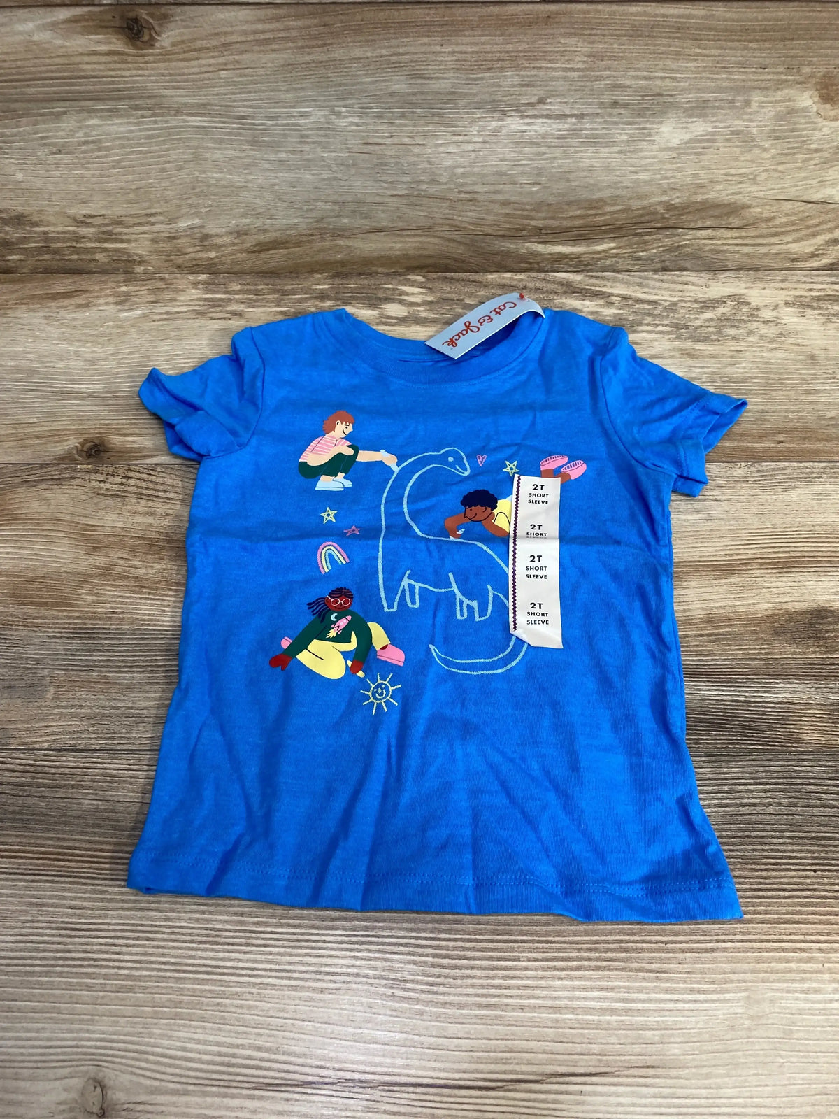 Flat-lay of blue Cat & Jack toddler T-shirt (2T) showing chalk-outline dinosaur and colorful child illustrations on wood background