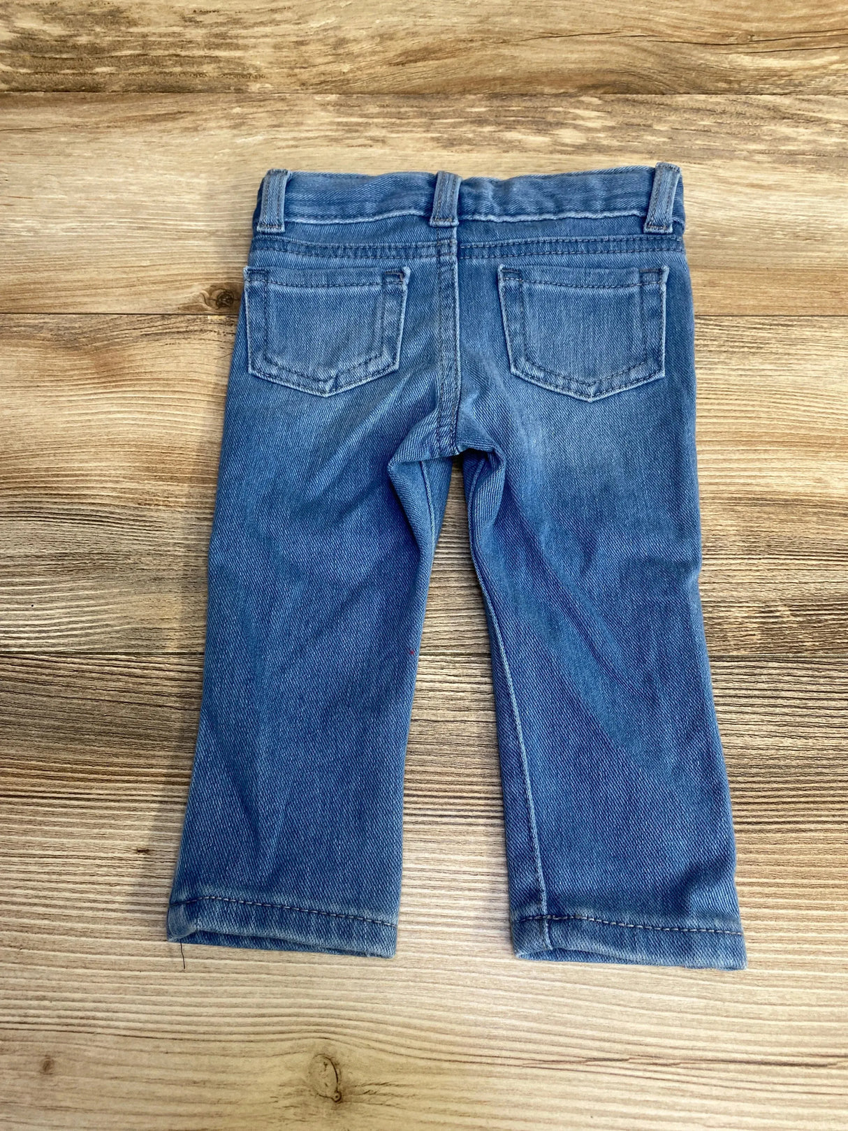 Back view of Cat & Jack baby jeggings in blue showing elastic waistband, back pockets, and straight legs on wood background