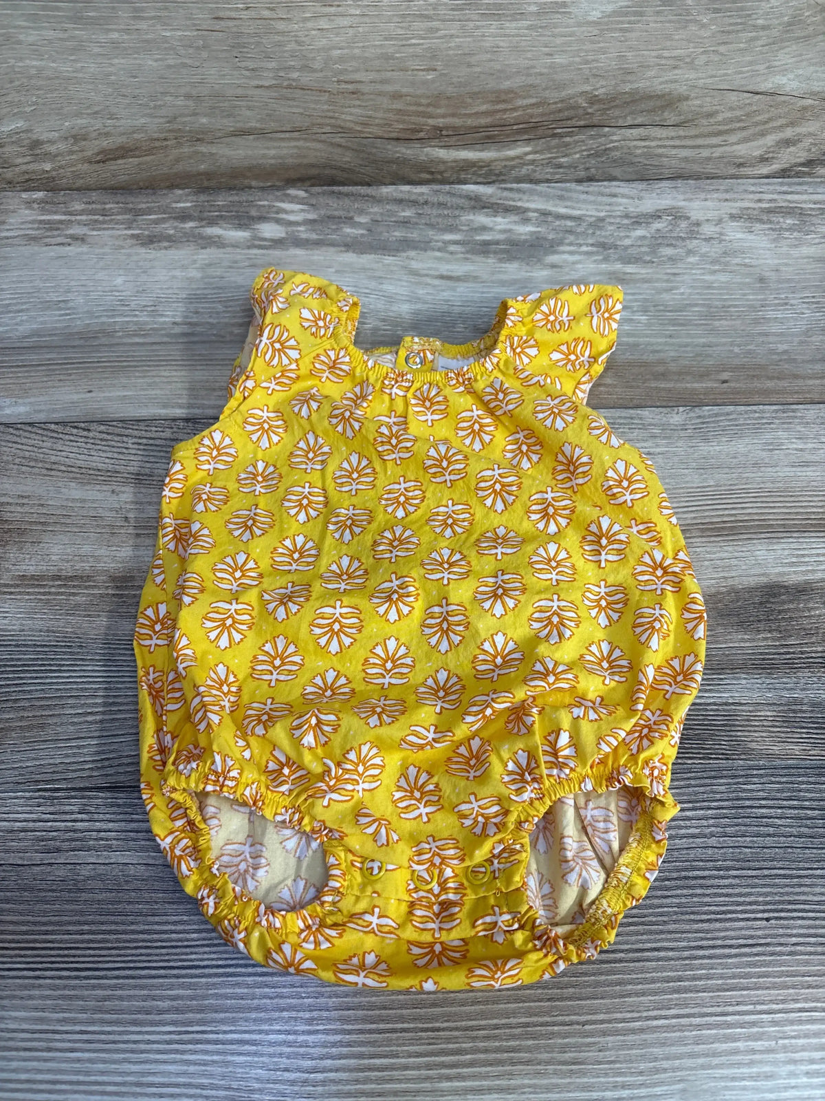 Flat lay of yellow Just One You romper, 3m, flutter sleeves, white-orange leaf print, snap crotch on light wood