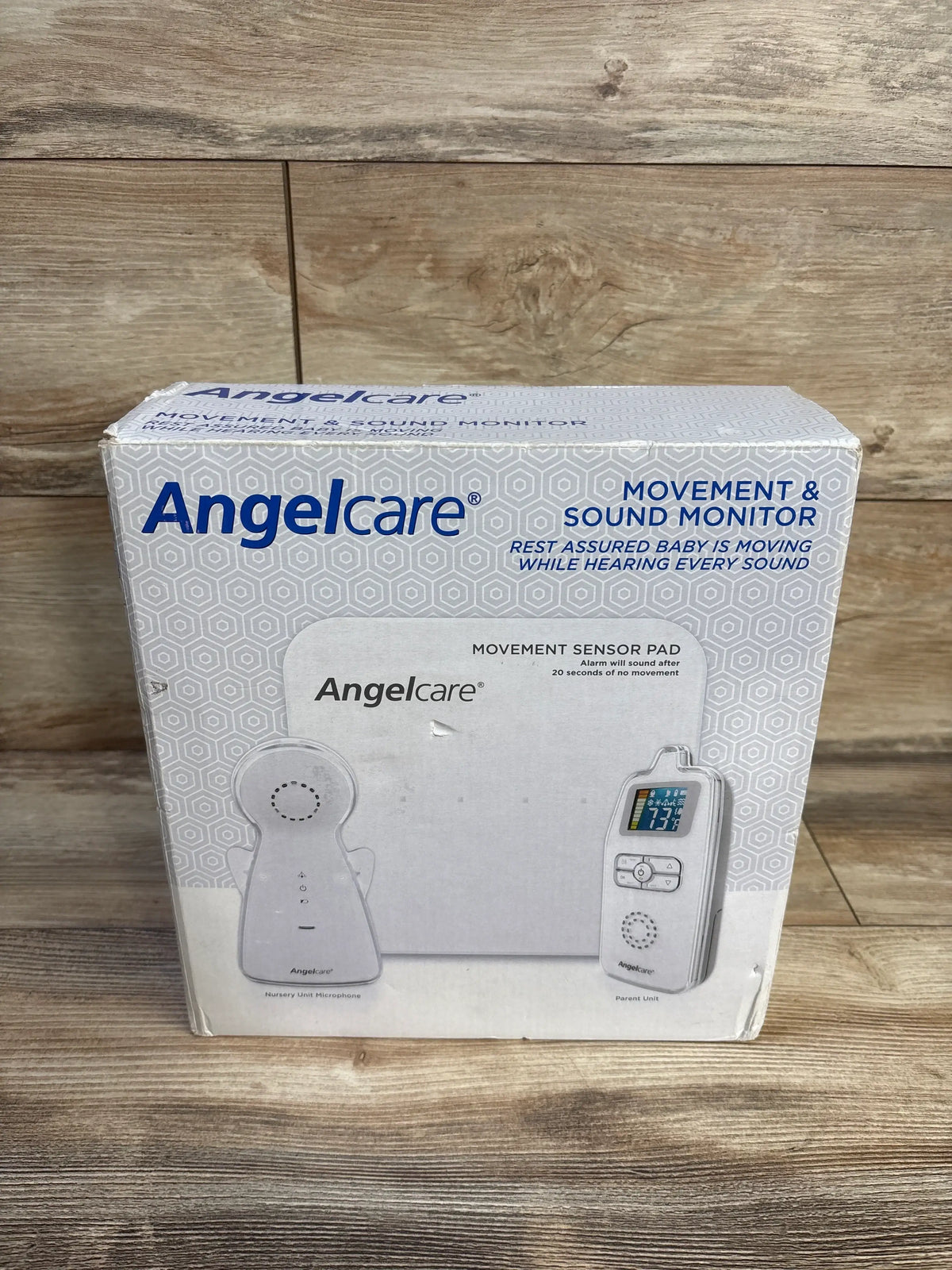 Front view of Angelcare Movement & Sound Monitor box showing movement sensor pad and parent unit on wood backdrop