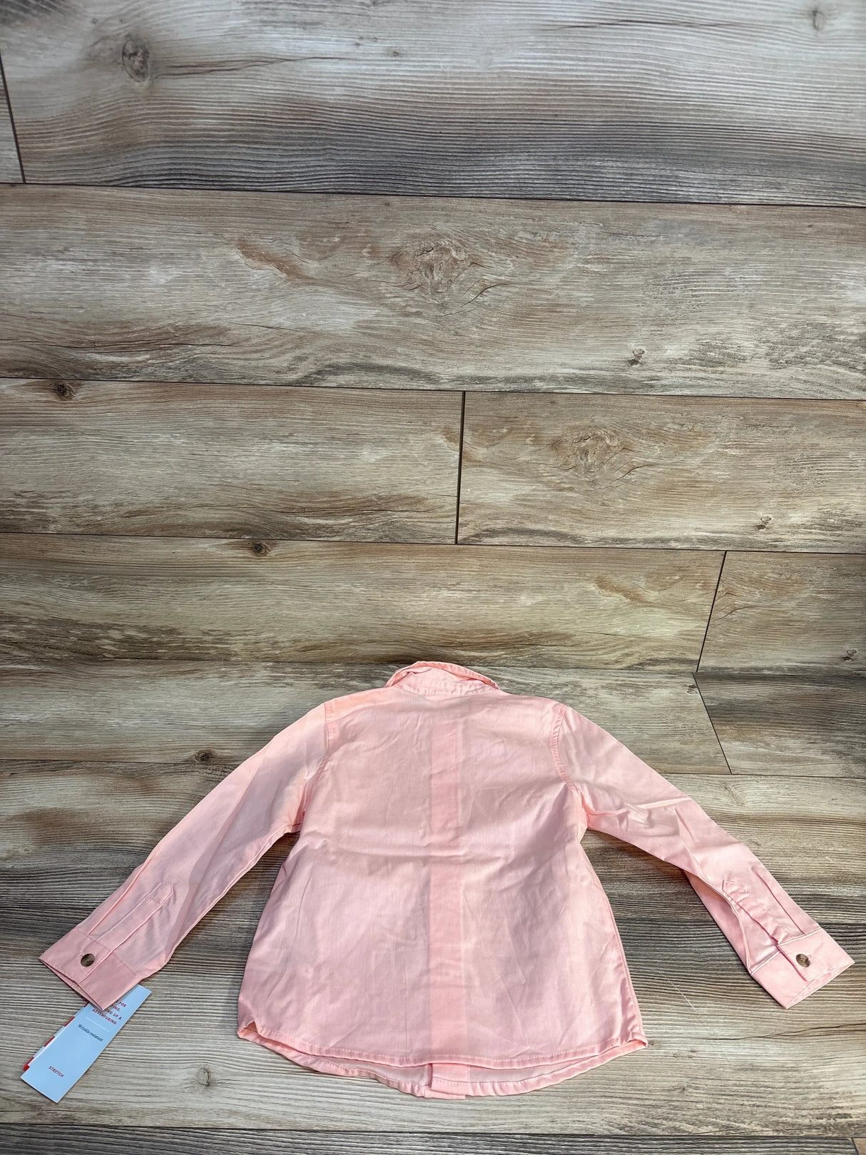 Light pink long sleeve button-up kids shirt laid flat on wood floor