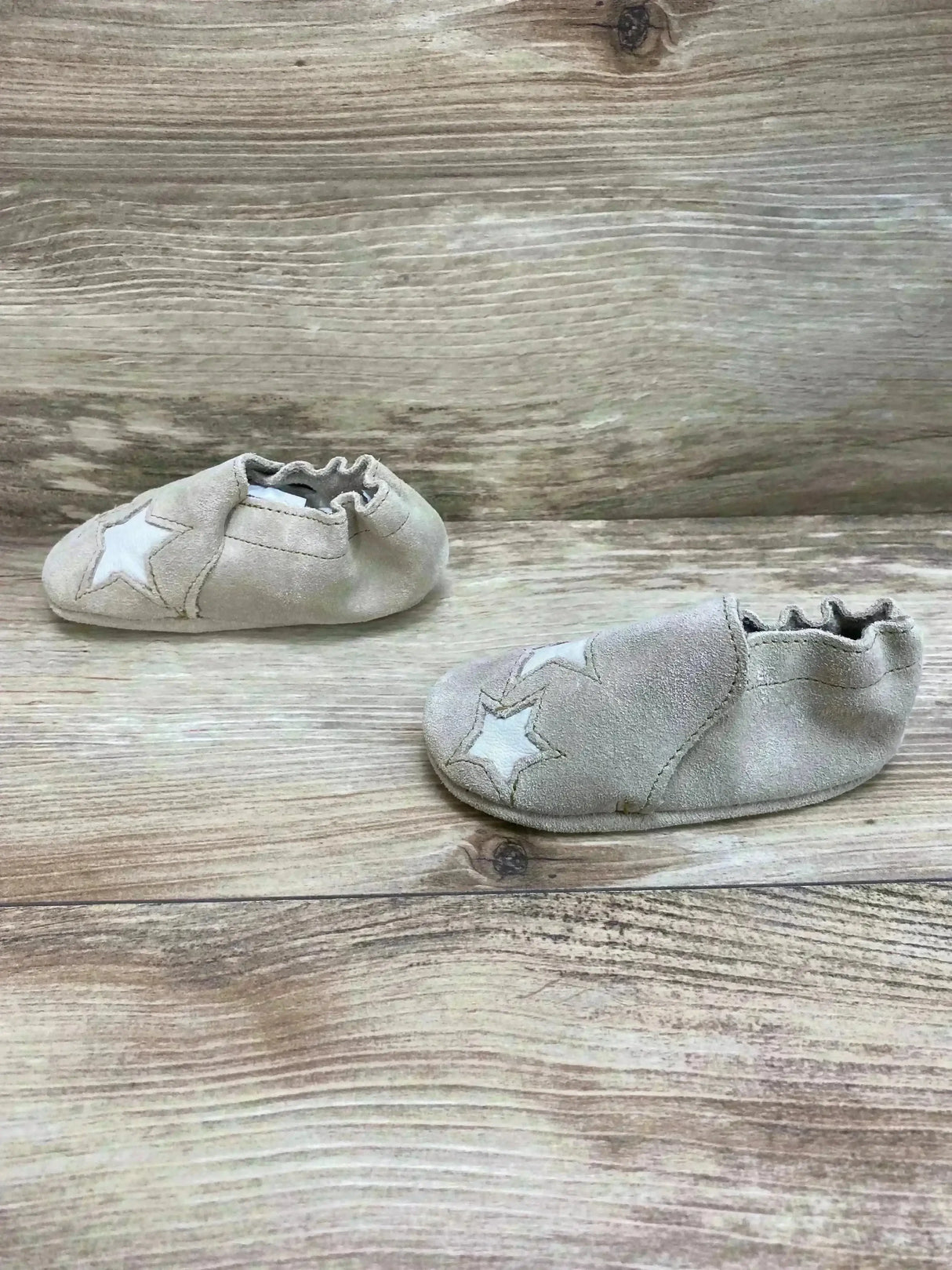Side view of tan Minnetonka infant booties showcasing white star appliqués on a wood surface