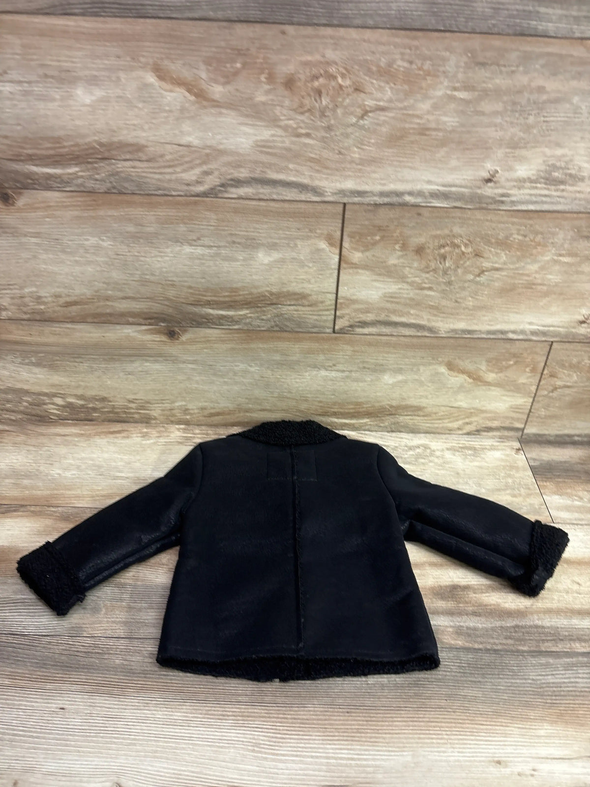 Back view of Urban Republic black faux leather moto jacket, size 3T, with fuzzy trim on collar, cuffs, and hem on wood floor