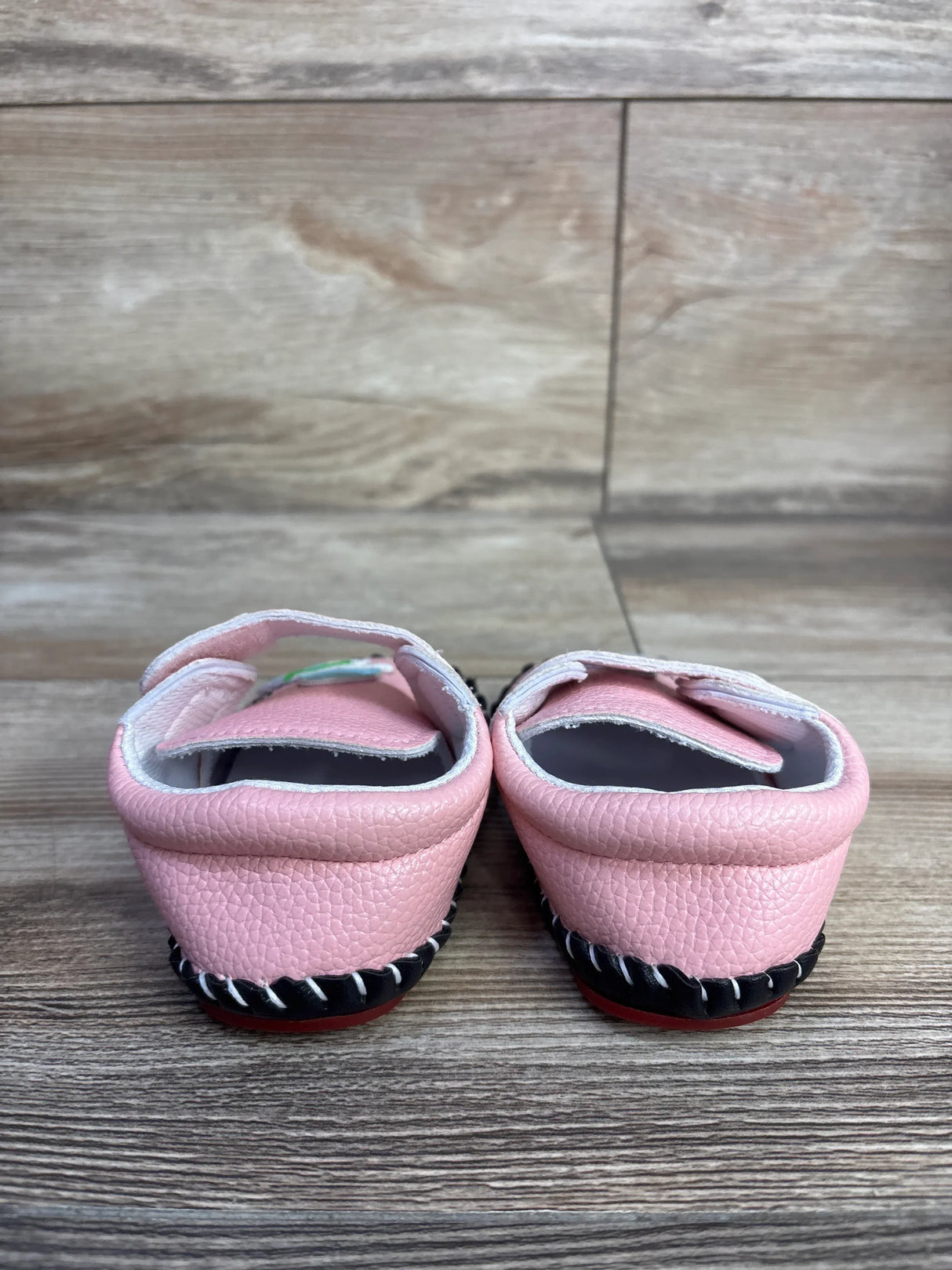 Rear view of pink toddler PU leather sneakers size 3C showing hard black sole with red tread and Velcro strap on wood floor