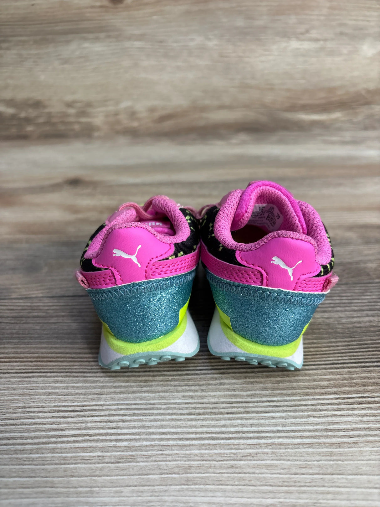 Pink and teal Puma kids' sneakers on wood floor, viewed from the back