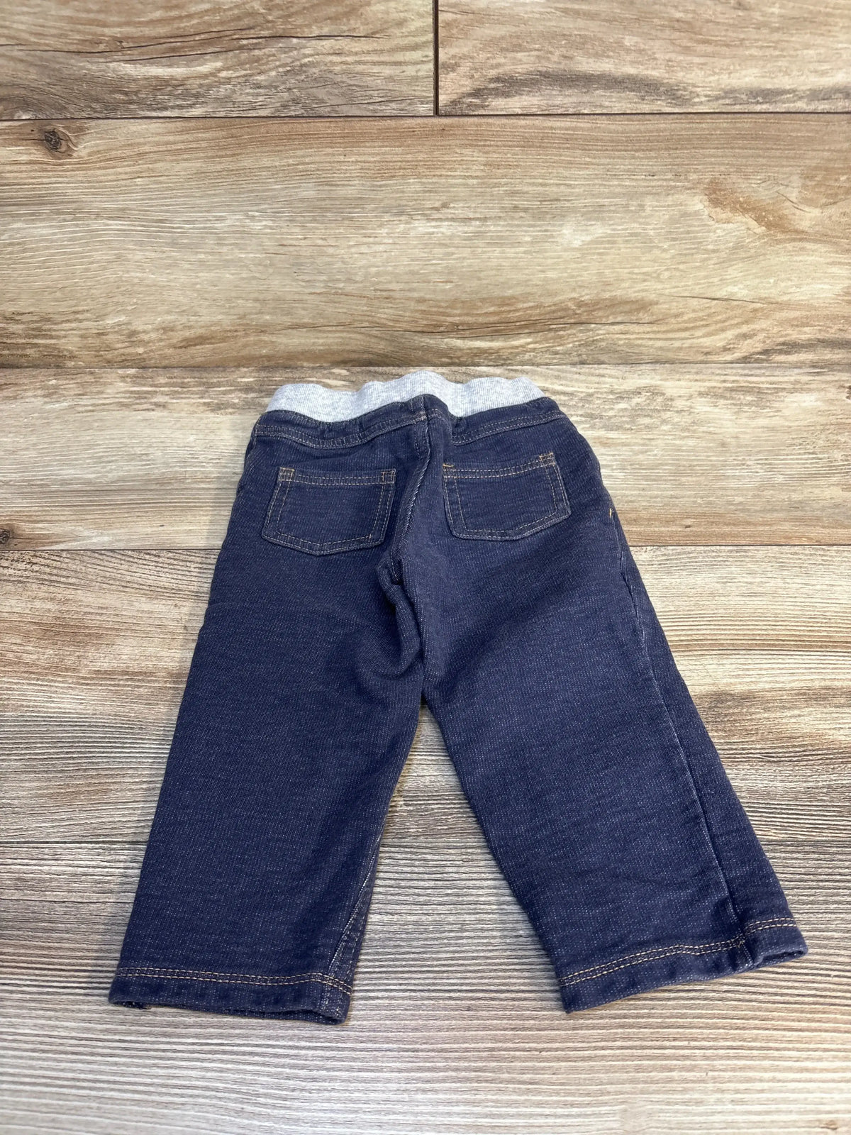 Baby or toddler denim pants with gray elastic waistband, back pockets, on wooden floor