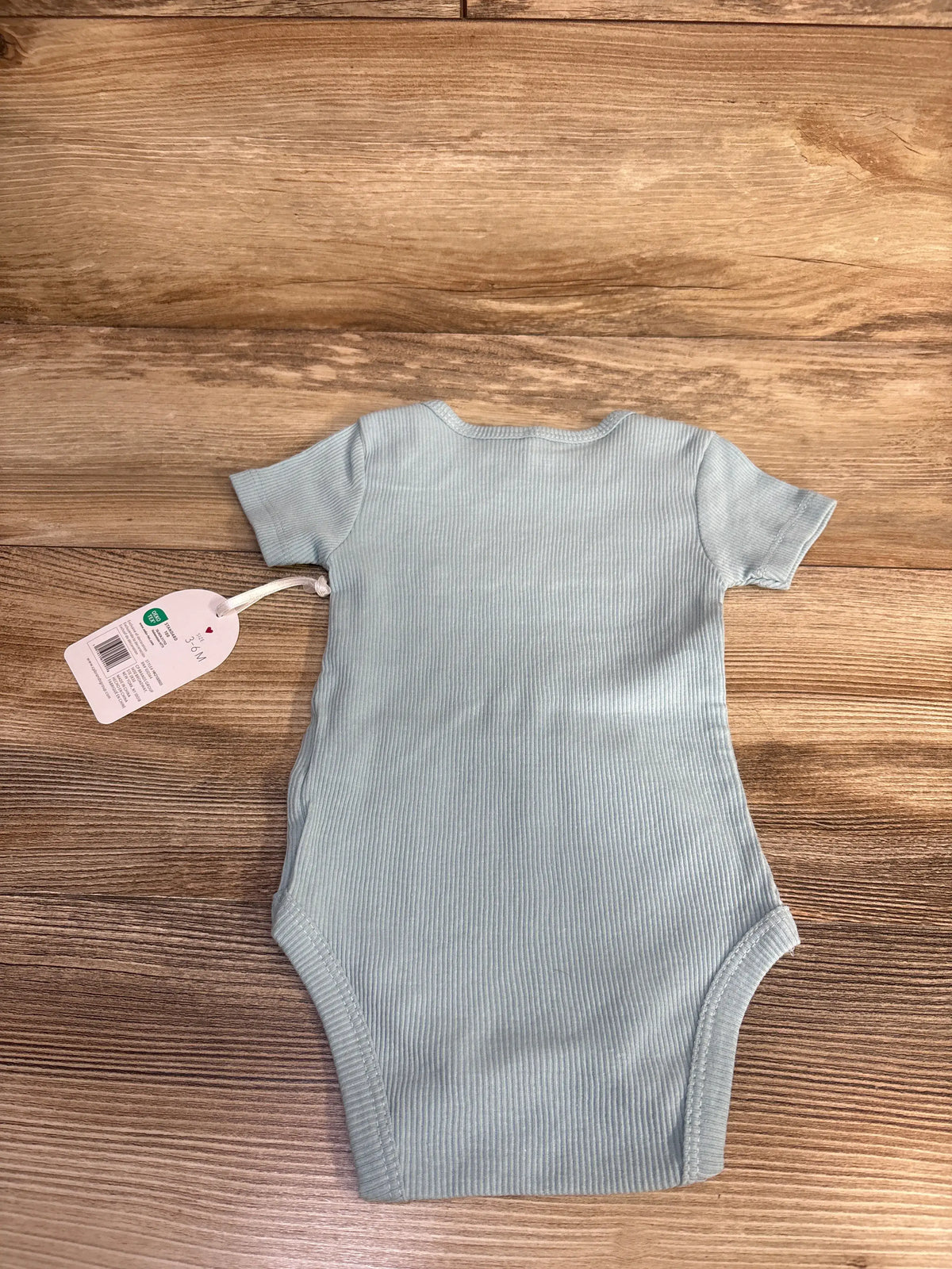 Front view of Kyle + Deena Daddy Loves Me A Ton blue ribbed bodysuit showcasing short sleeves on a wooden background