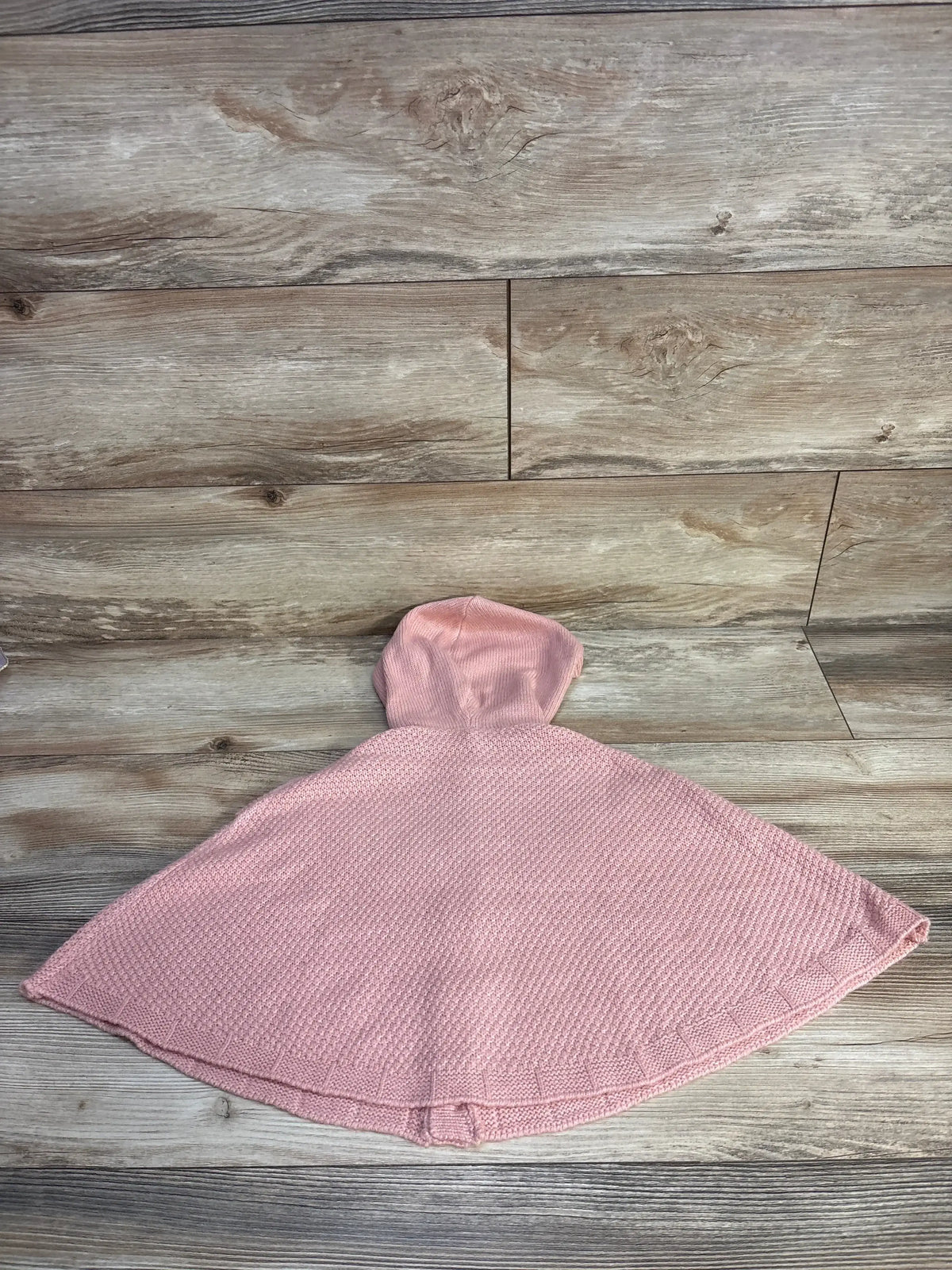 Pink knit hooded baby poncho on wood background