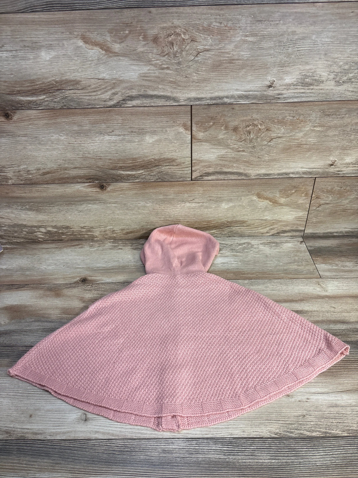 Pink knit hooded baby poncho on wood background