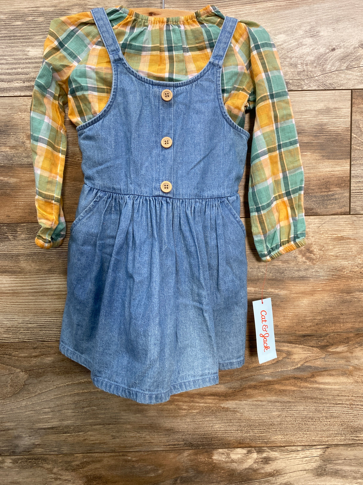 Girls long sleeve plaid shirt with yellow and green tones, layered under blue denim dress with wooden buttons
