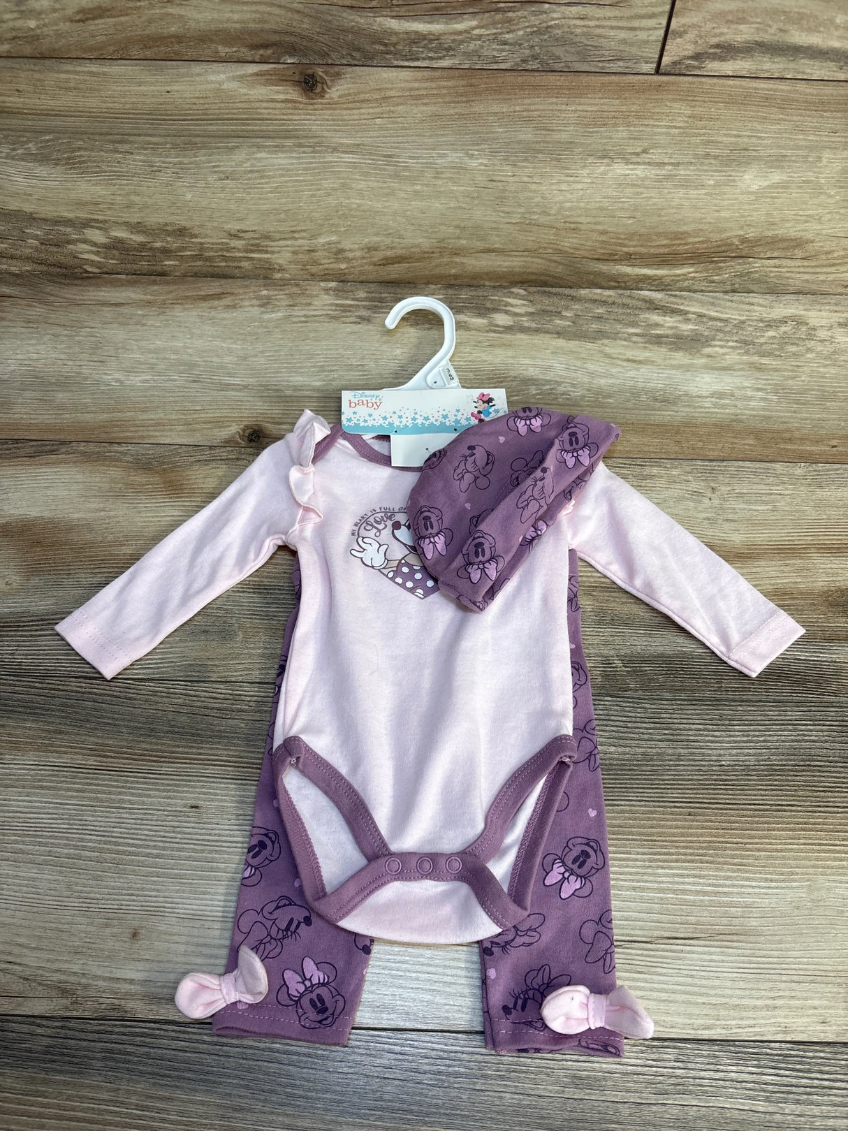 Disney Baby Minnie Mouse 3pc outfit with pink ruffle bodysuit, purple print pants, and matching hat on hanger