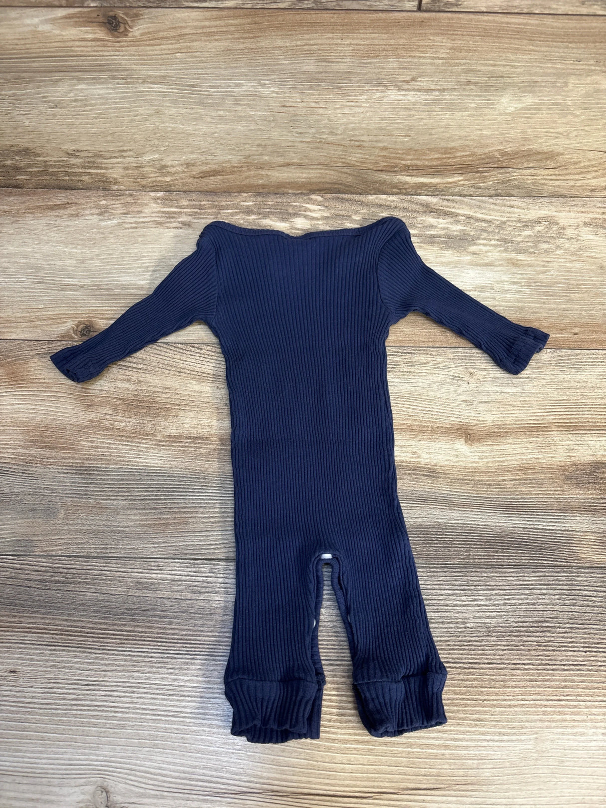 Navy blue ribbed baby onesie with long sleeves and snap closures, laid flat on wood floor