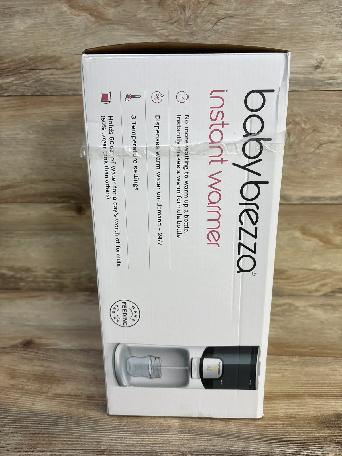 Front of Baby Brezza bottle warmer box showing instant warmer text and features, on demand warm water and 3 temps, on wood background