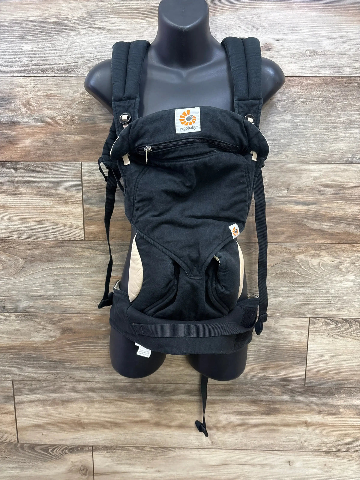Front view of Ergobaby Four Position 360 carrier with padded shoulder straps, zippered pocket and beige accents on wood background