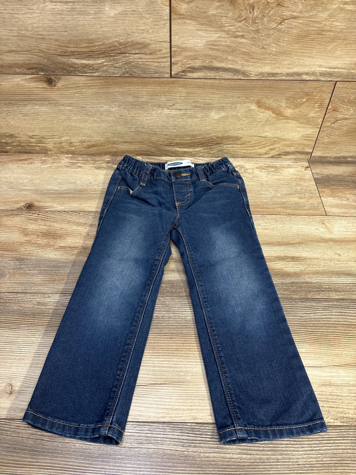 Flat lay of Old Navy straight blue toddler jeans showing elastic waistband and slight knee fading on wood floor background