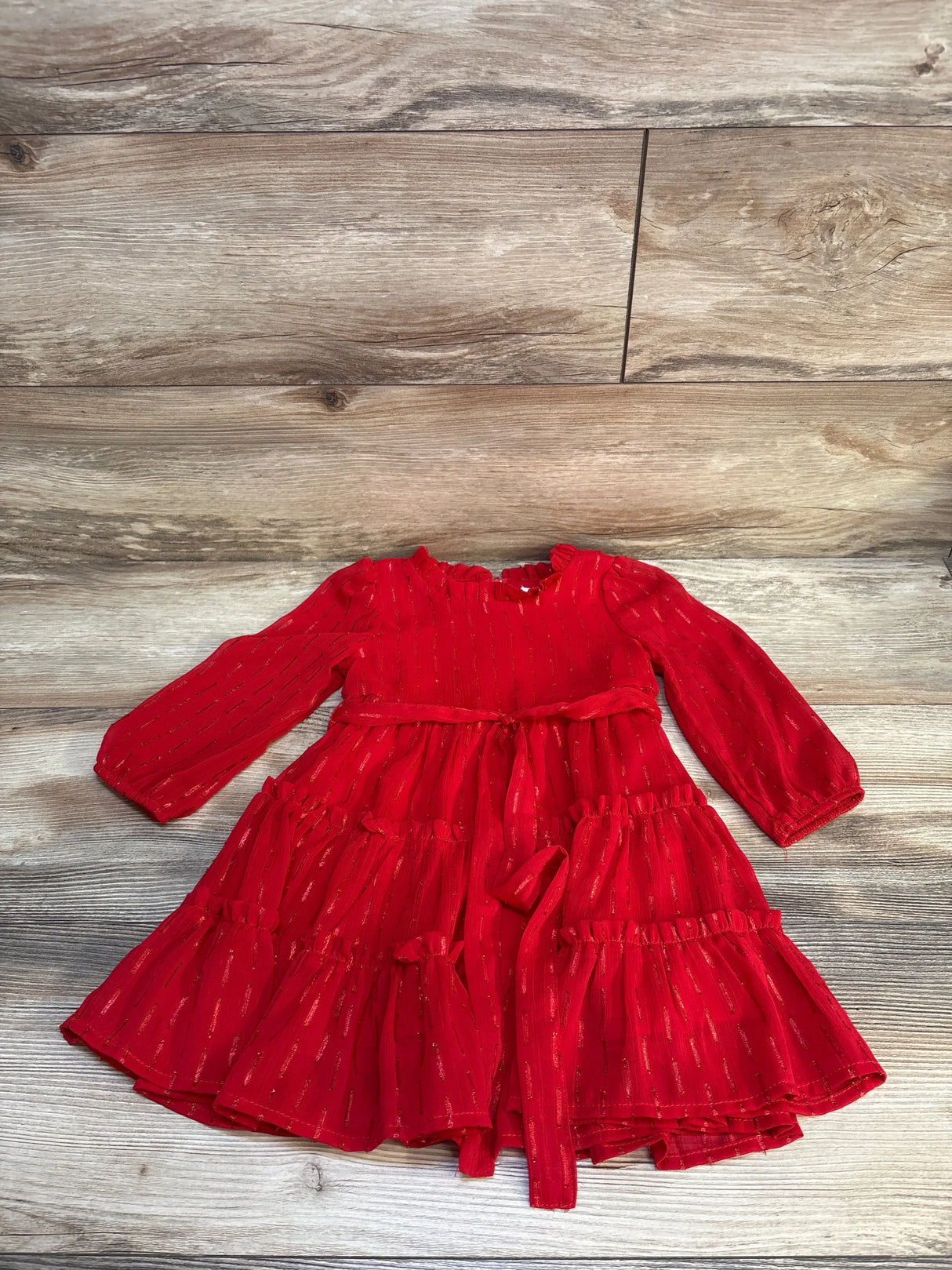 Red long sleeve toddler dress with ruffle skirt and gold accents on wood background
