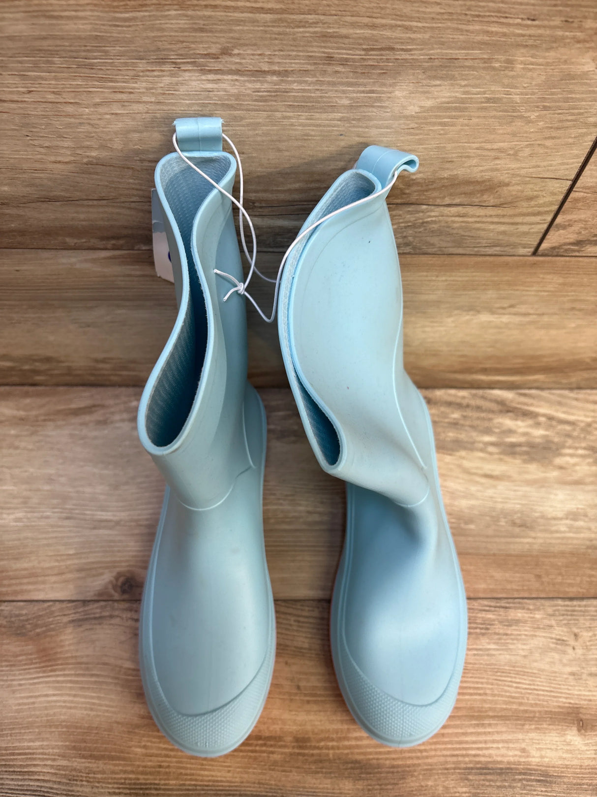 Light blue children's rain boots on wood floor, kids rubber footwear, top view