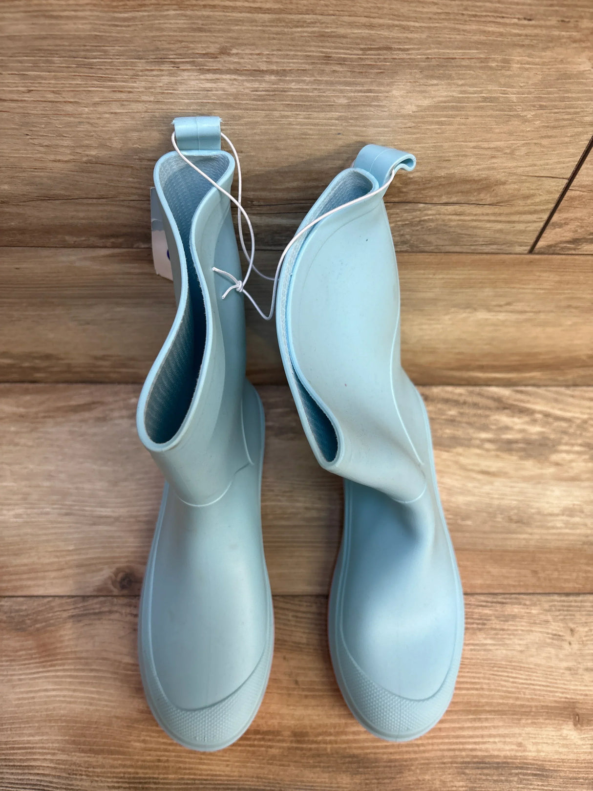 Light blue children's rain boots on wood floor, kids rubber footwear, top view