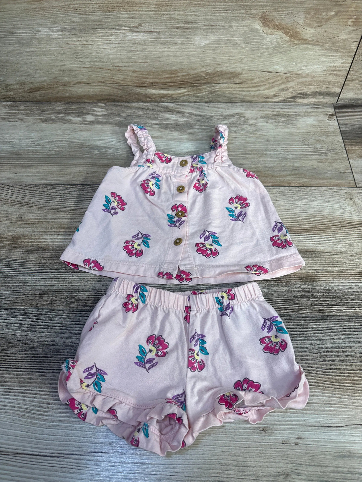 Front view of Carter’s pink tank top and shorts set showcasing floral print and ruffled hems on a wood background