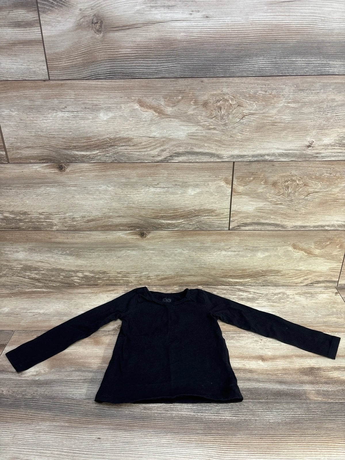 Front view of Children’s Place long sleeve shirt in black, size 3T, showcasing long sleeves with a wood-look background
