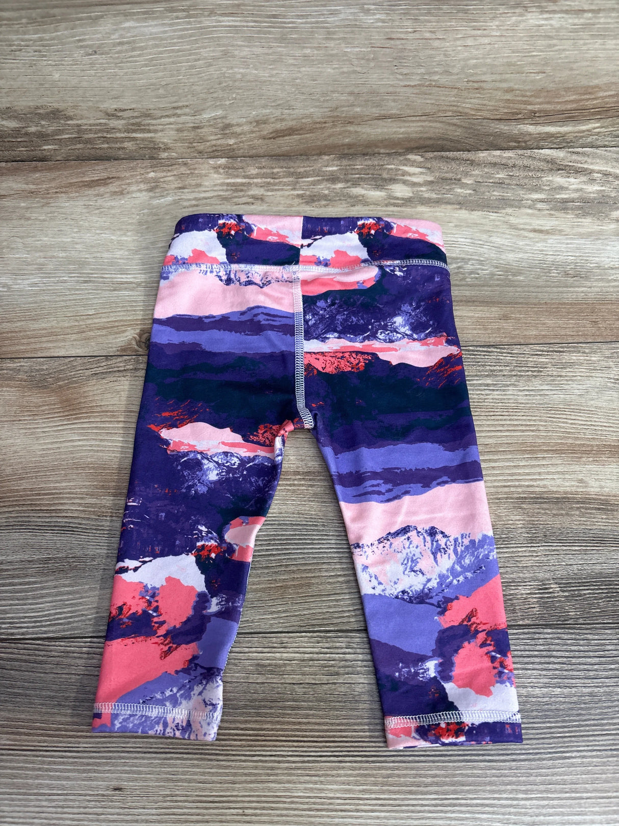 Colorful baby leggings with mountain print, purple and pink hues, on wooden surface