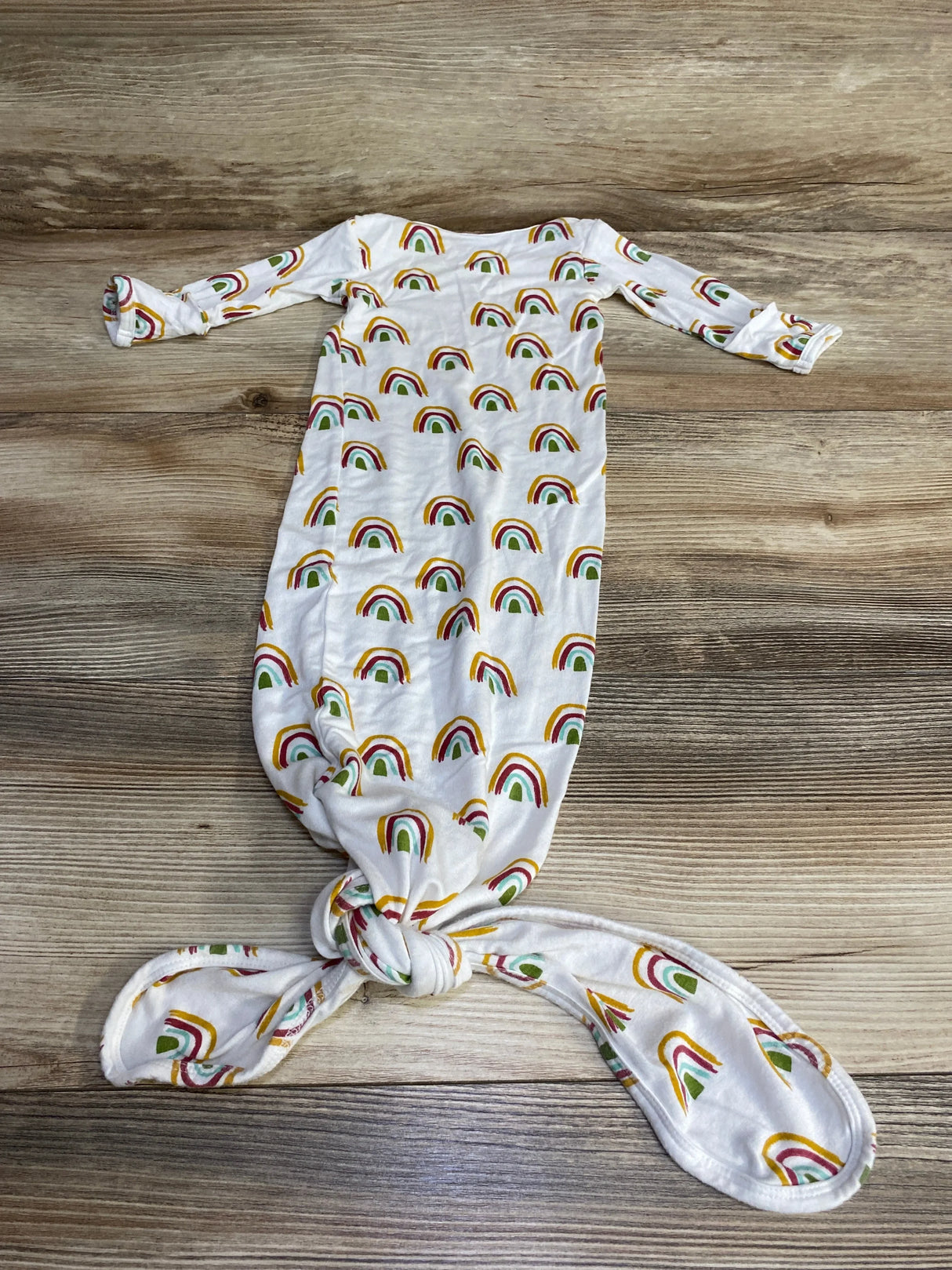 Flat lay of Emerson and Friends white knot gown showcasing rainbow print, long sleeves and knotted bottom on wood background