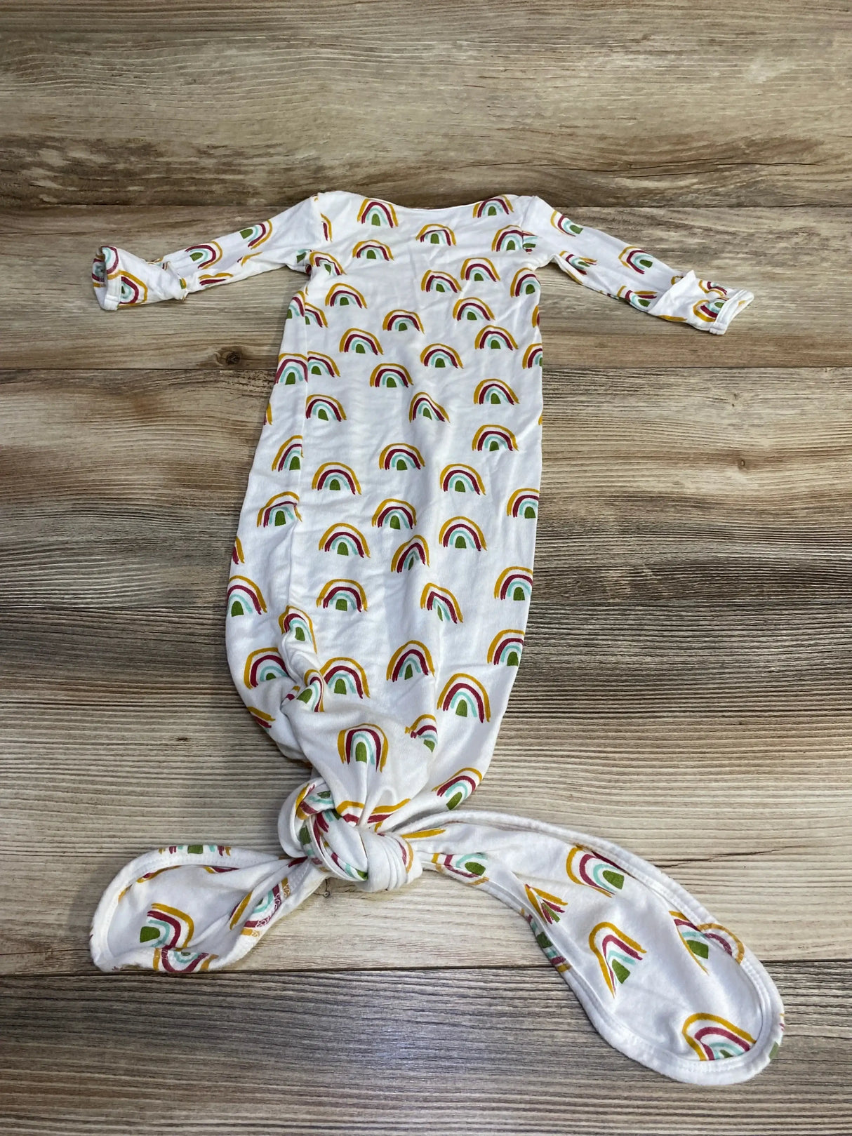 Flat lay of Emerson and Friends rainbow knot gown in white showcasing rainbow print with knotted bottom and long sleeves on wood plank floor
