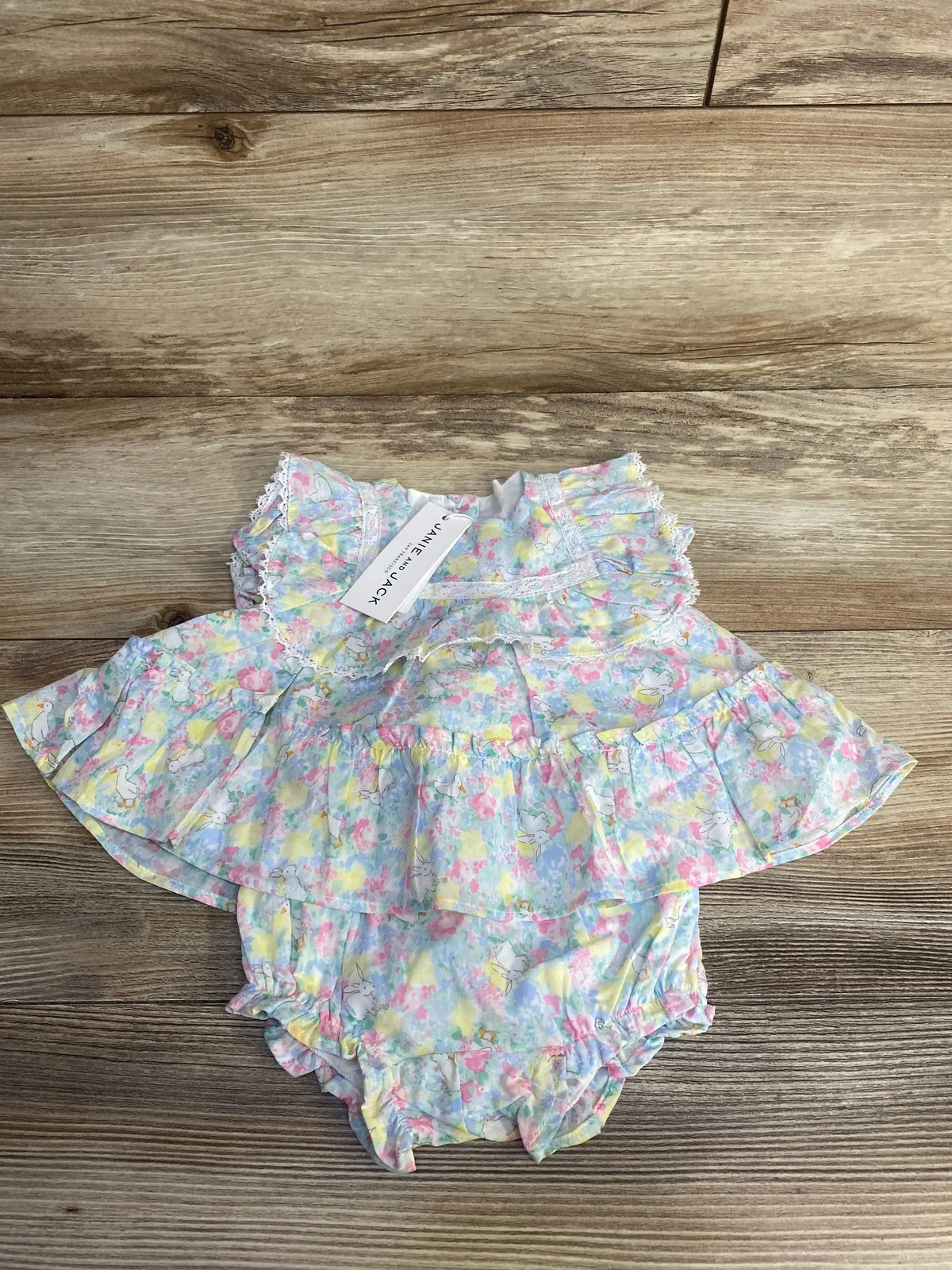 Top-down view of Janie and Jack 2-piece pastel floral bunny baby set with ruffled lace-trim peplum top and matching ruffled bloomers on wood background
