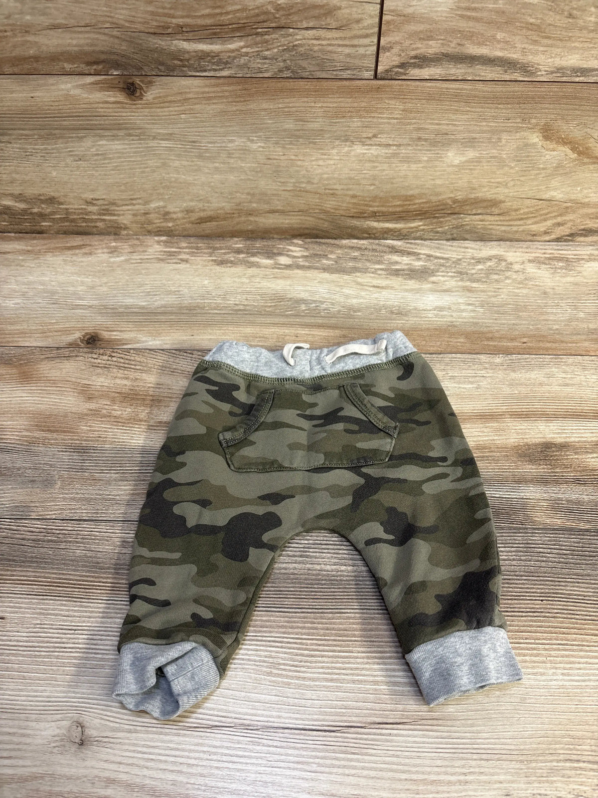 Flat lay of Baby Gap camo drawstring joggers with front kangaroo pocket, gray elastic waistband and cuffed ankles on wood background