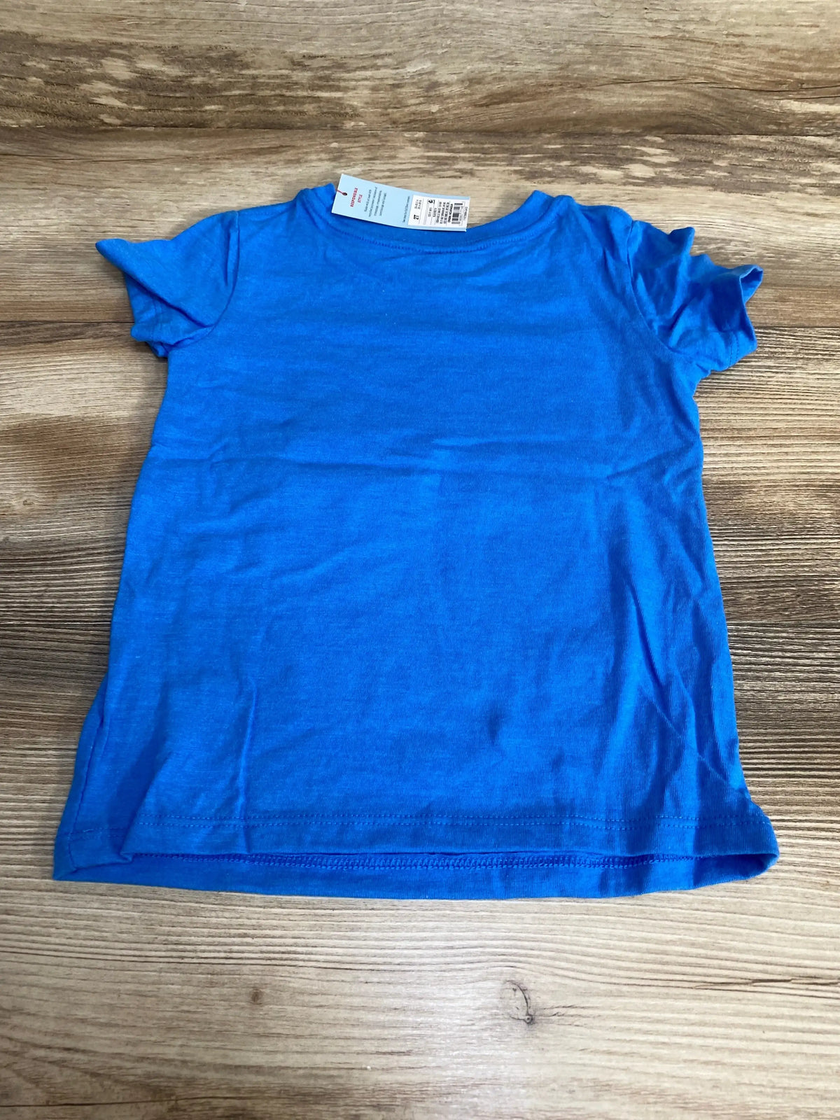 Top down flat lay of Cat and Jack toddler blue tee size 2T with retail tag on wood background