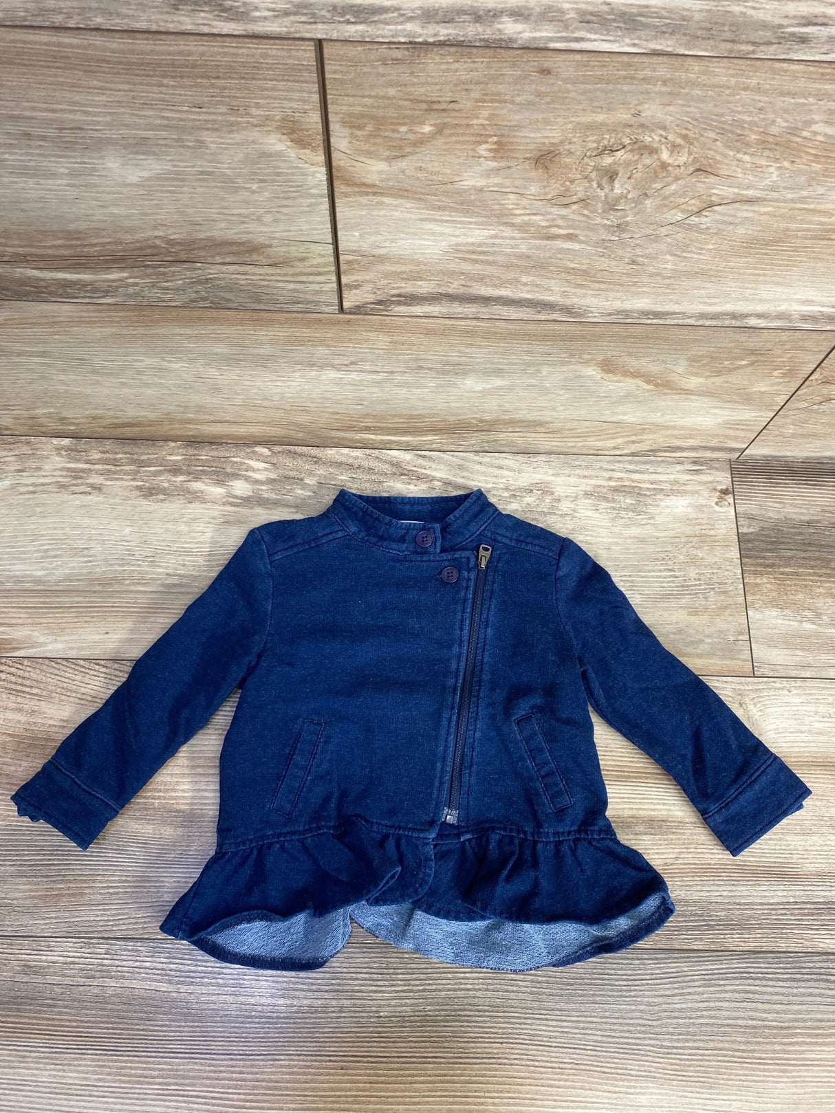 Navy blue toddler jacket with ruffle hem, front zipper, and button details on wood floor