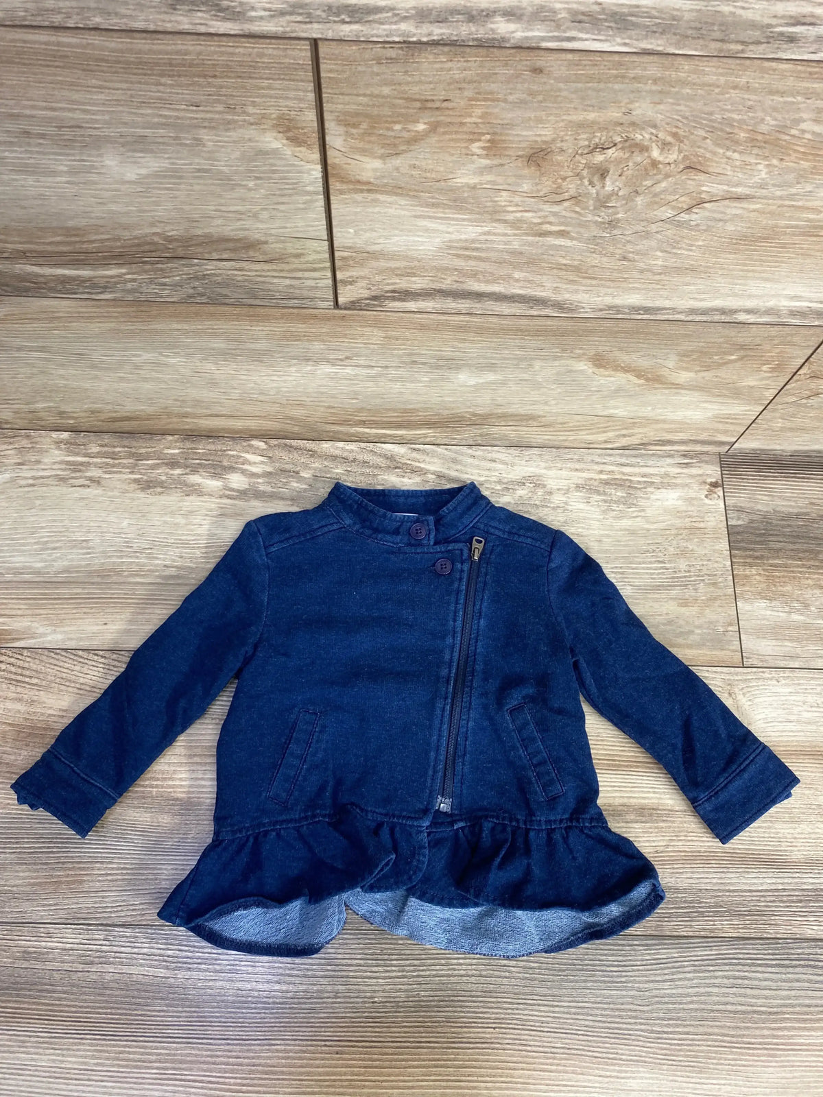 Navy blue toddler jacket with ruffle hem, front zipper, and button details on wood floor