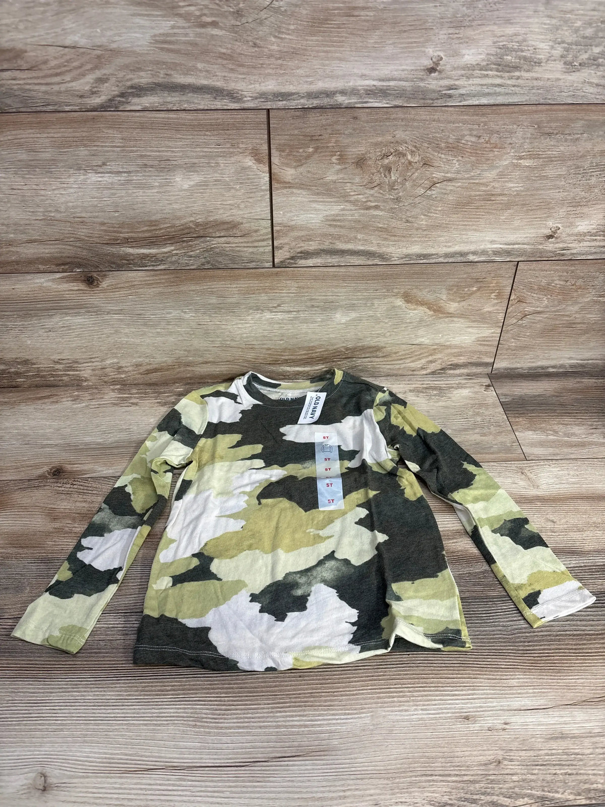 Kids long sleeve camo shirt with green, white, and yellow pattern on wood background